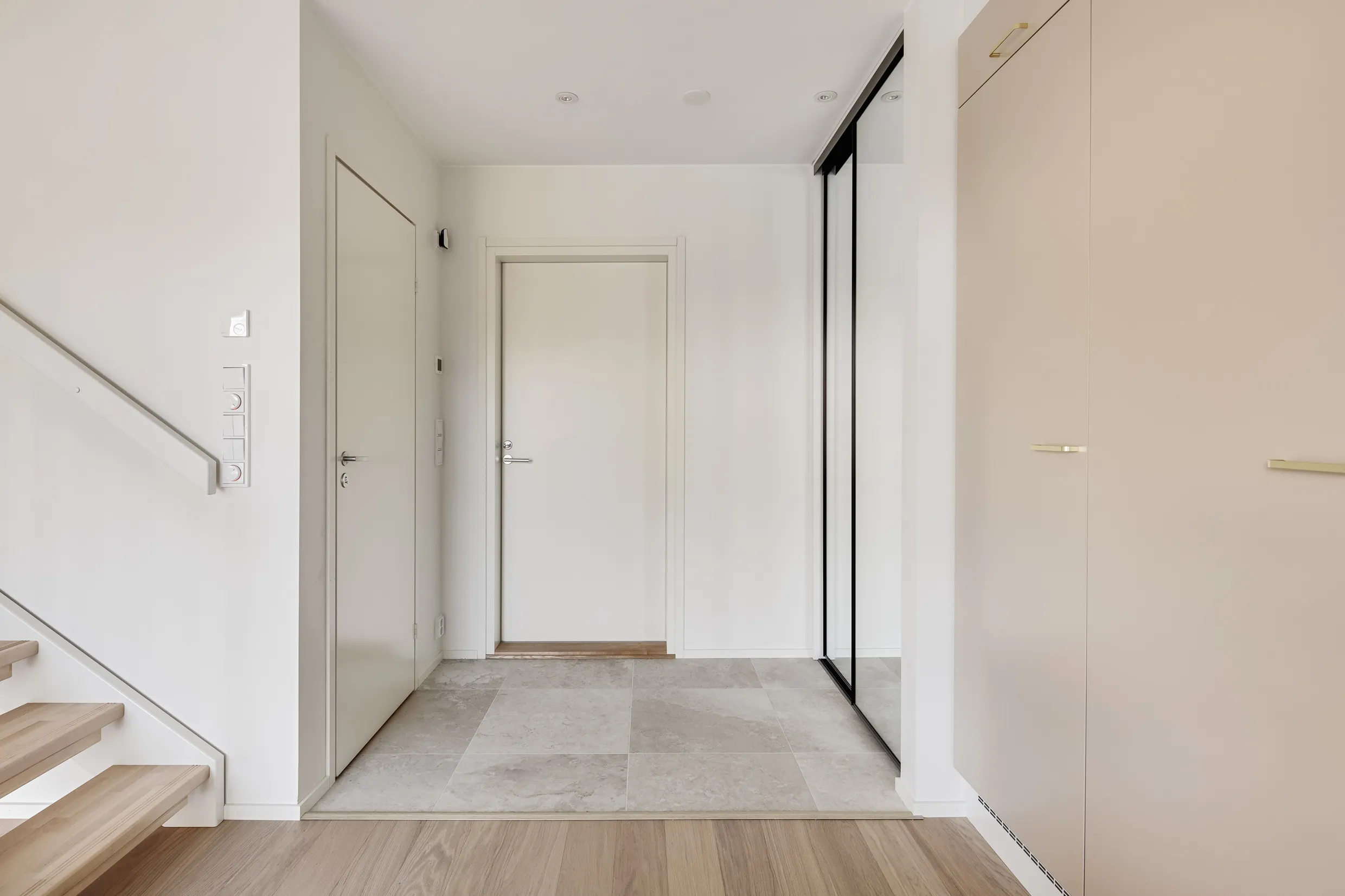 Vaaleassa eteisessä on valkoinen ovi, peililiukuovi, beige kaappi ja puuportaat. Lattiat ovat puuta ja laattaa.