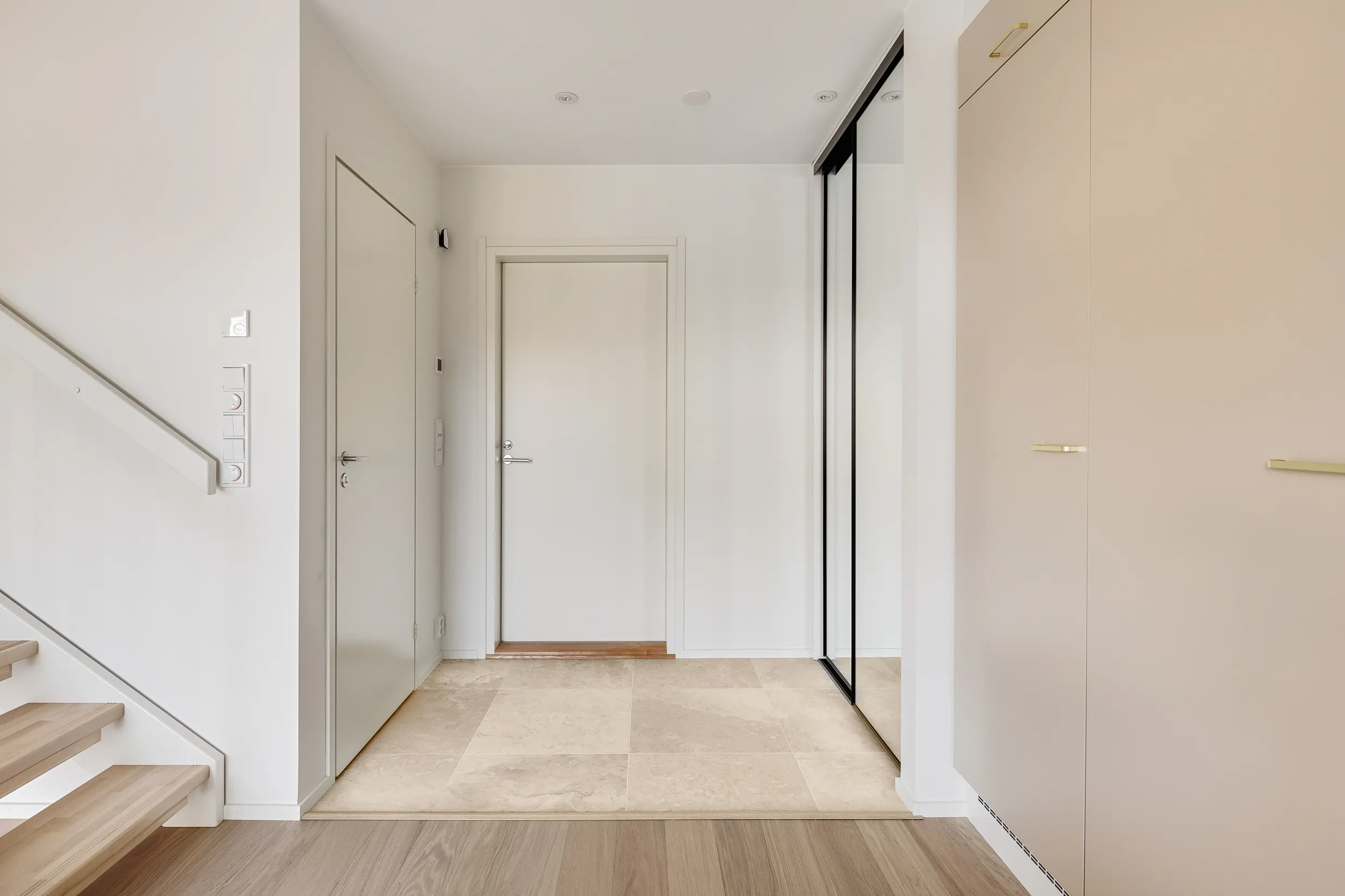 Vaaleassa eteisessä on valkoiset seinät, vaaleat laatat ja puuportaat. Peililiukuovi ja vaaleanpunainen kaappi.