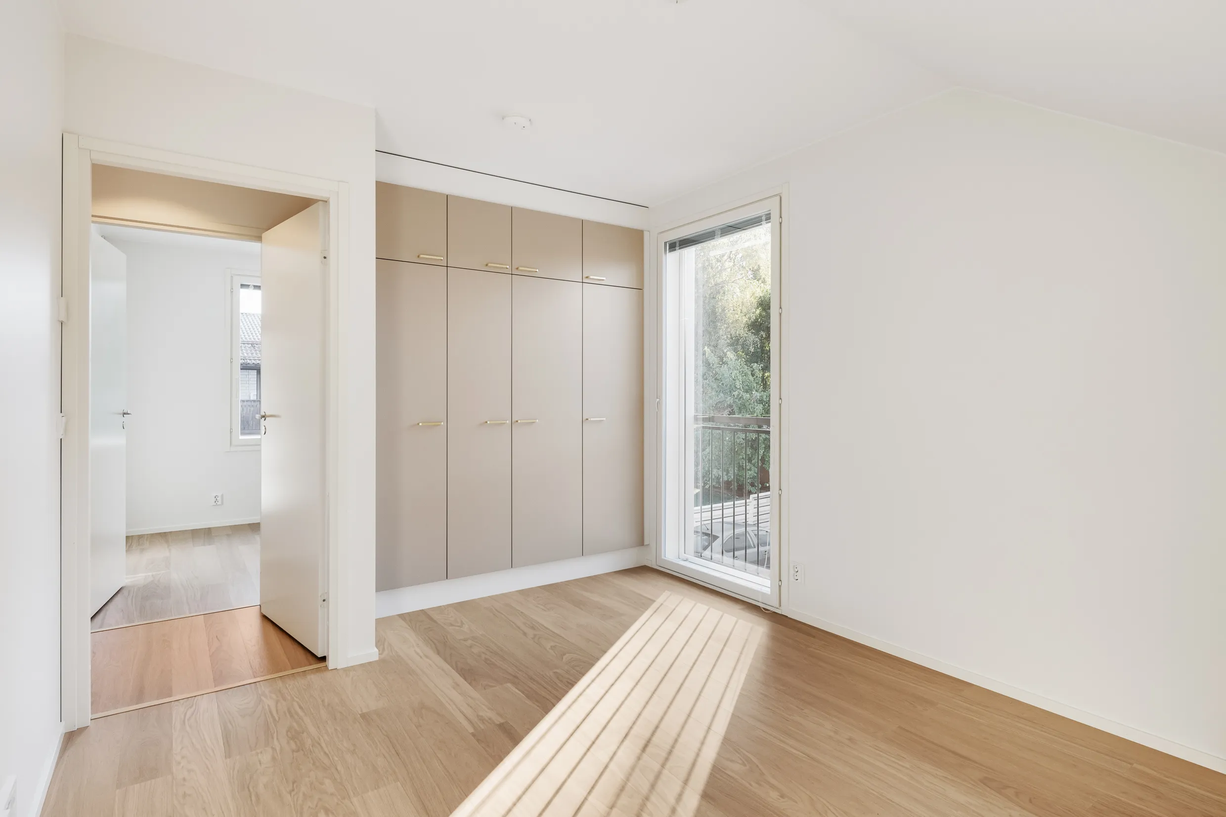 Vaalea huone, jossa on vaatekaappi, ikkuna ja puulattia.