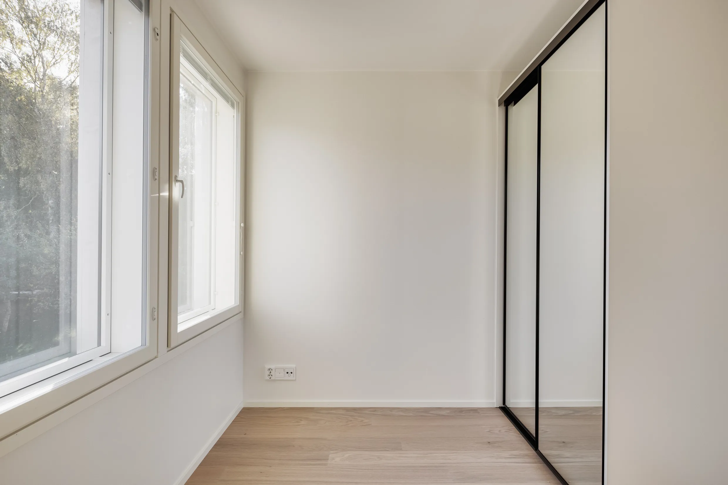 Vaalea huone, ikkuna, liukuovikaappi ja puulattia.