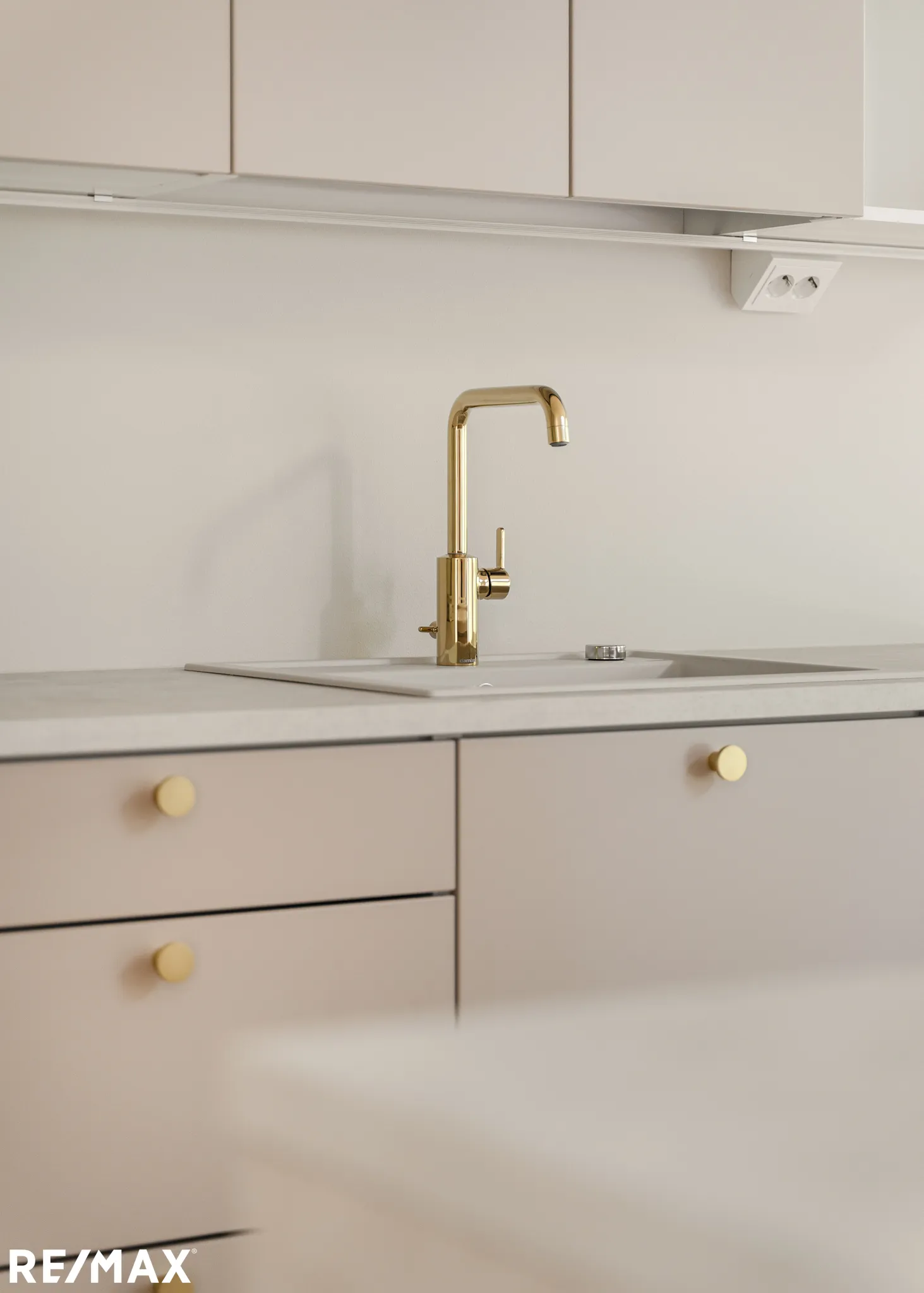 Vaalean keittiön kultainen hana, kaapit ja RE/MAX-logo.
