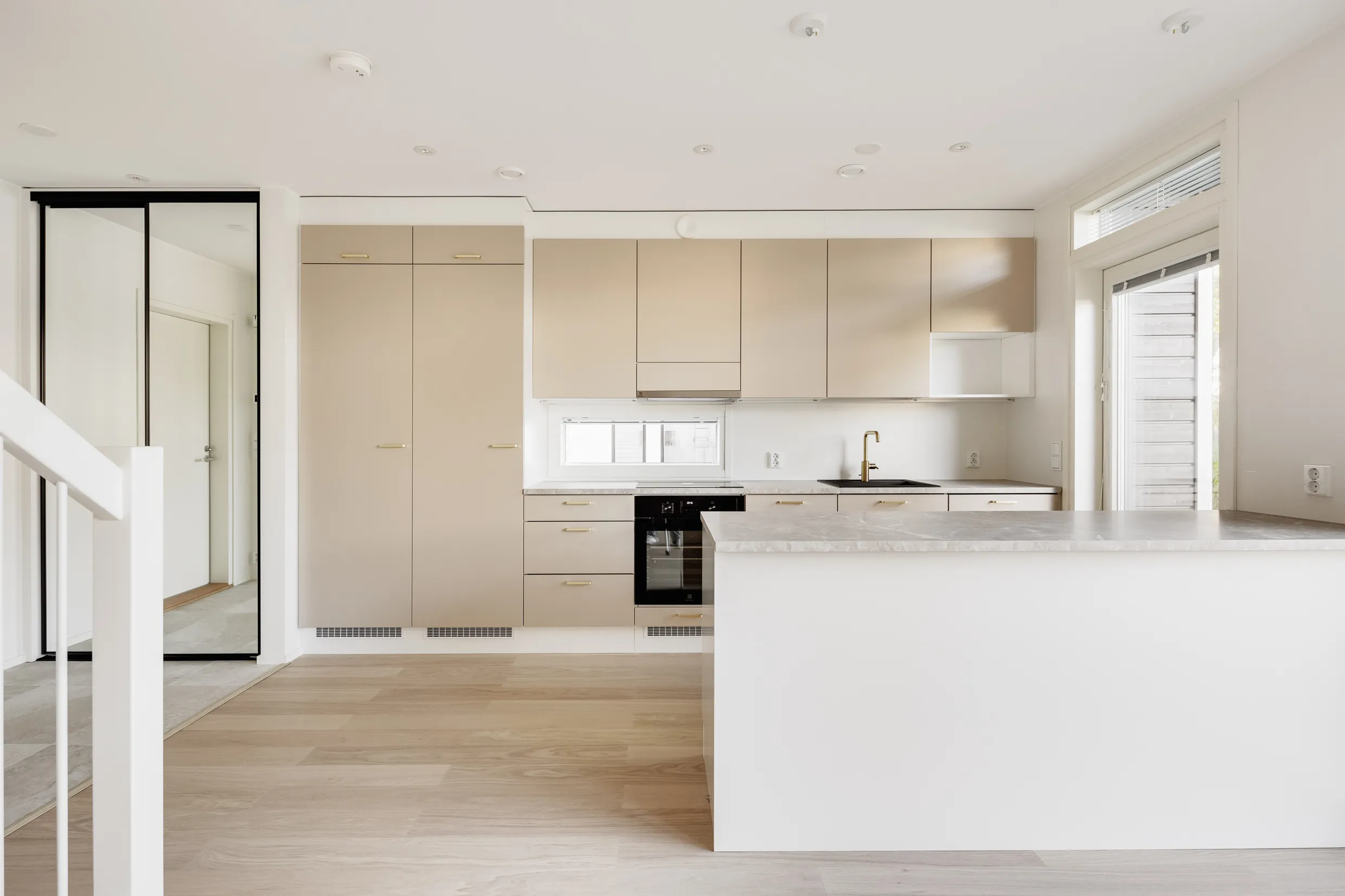 Vaalean keittiön sisustus, jossa on puulattia, beigejä kaappeja ja valkoinen saareke.