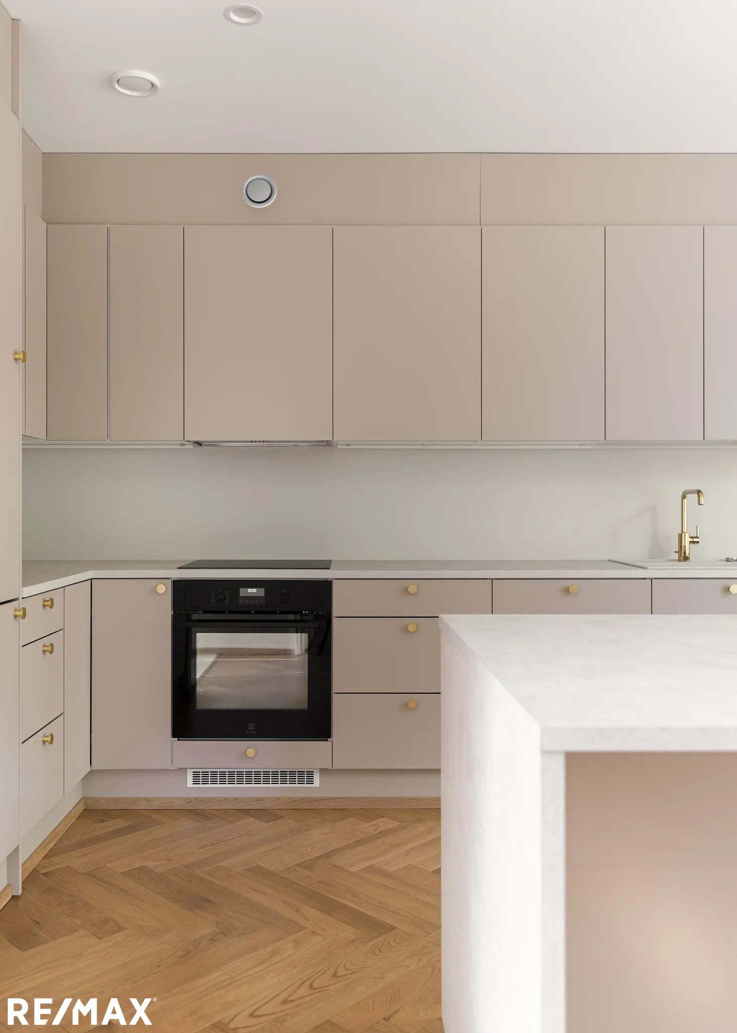 Vaaleanruskea keittiö, jossa on puulattia, kultaiset vetimet ja valkoinen työtaso.