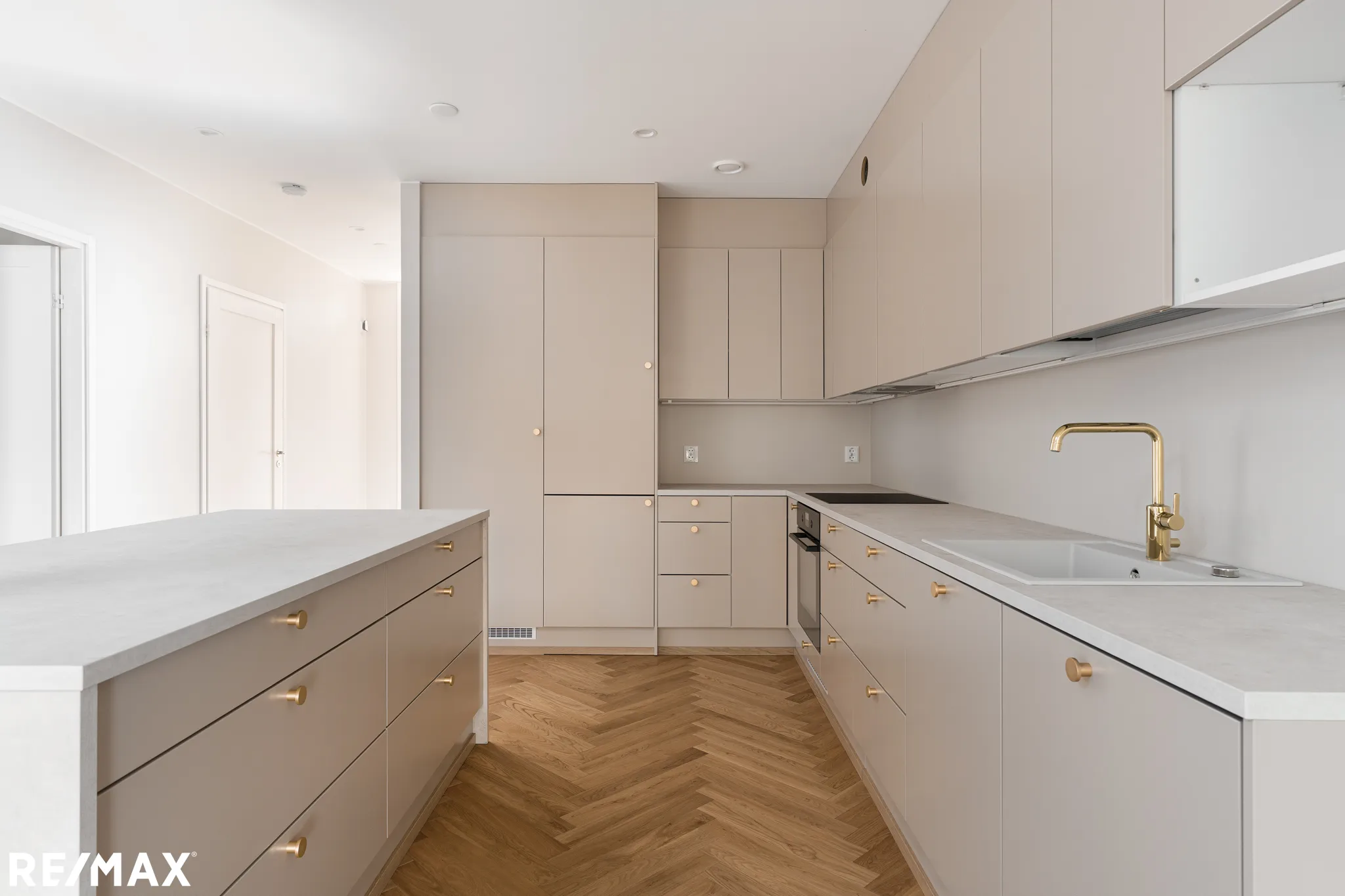 Vaalean keittiön sisustus, jossa on saareke, parkettilattia ja kultaiset hanat.