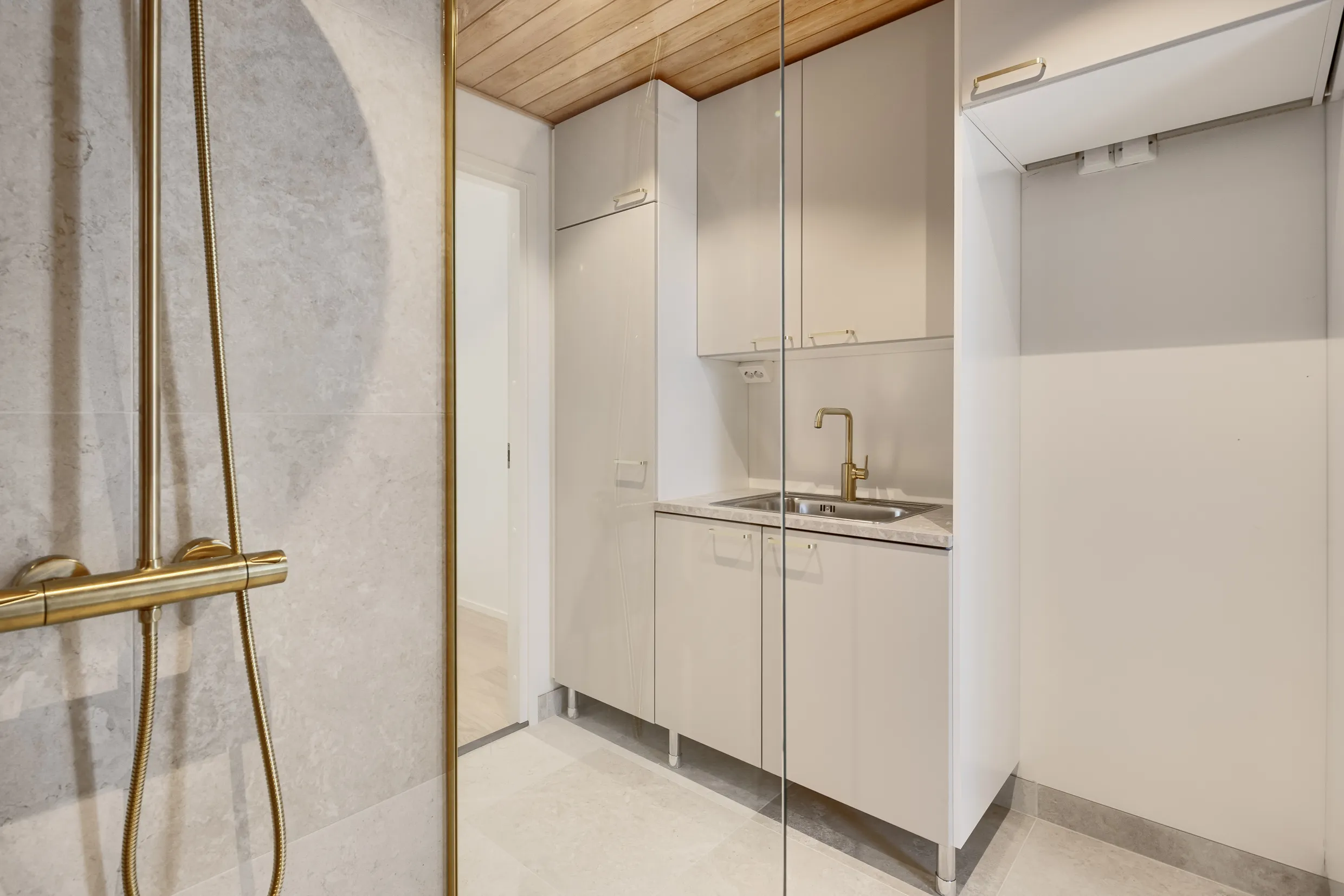 Kylpyhuoneen kuvaus: kultainen suihku, valkoiset kaapit, puinen katto ja marmorilattia.