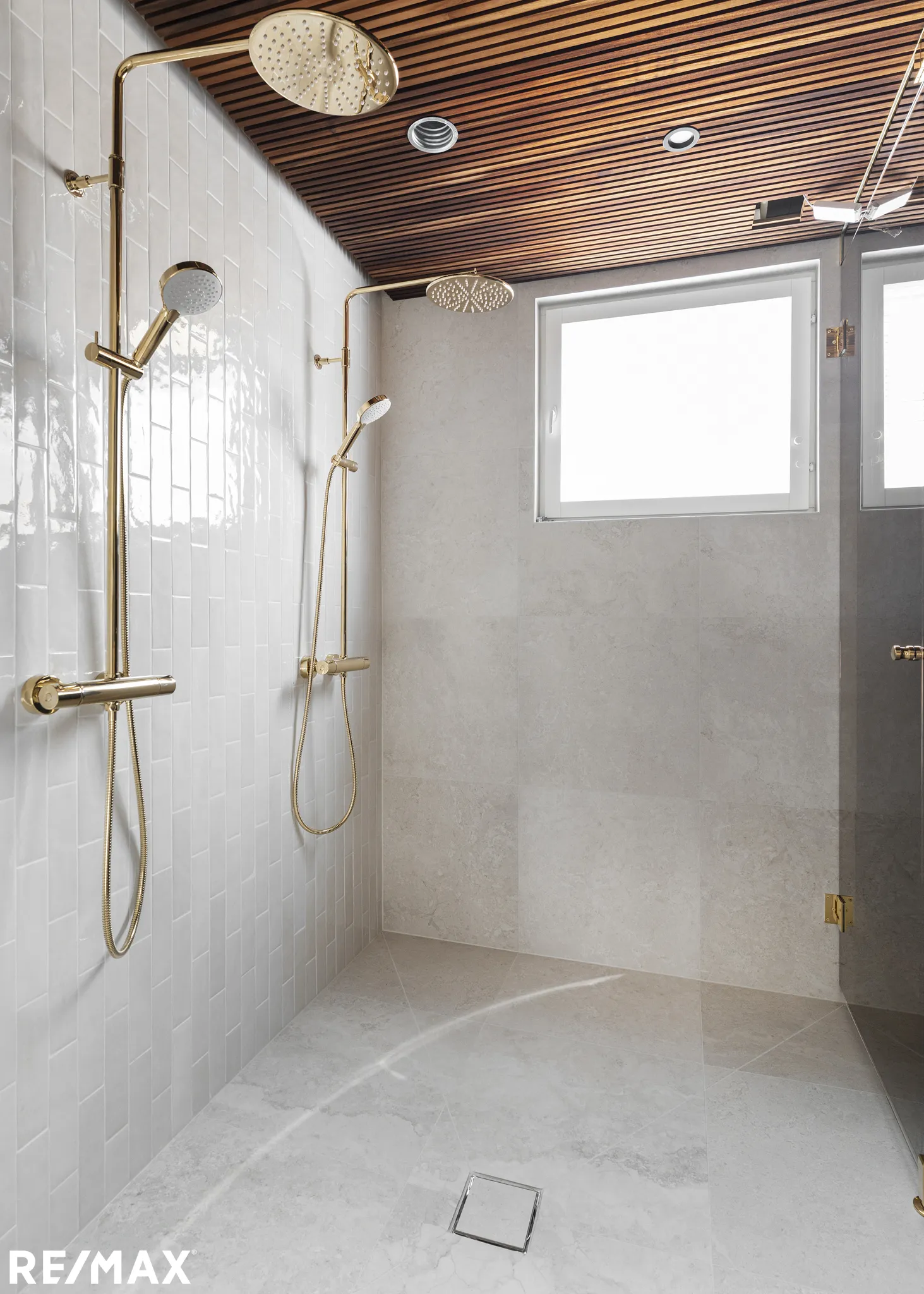 Moderni kylpyhuone kultaisilla suihkuilla, puinen kattopaneeli ja valkoiset seinälaatat.