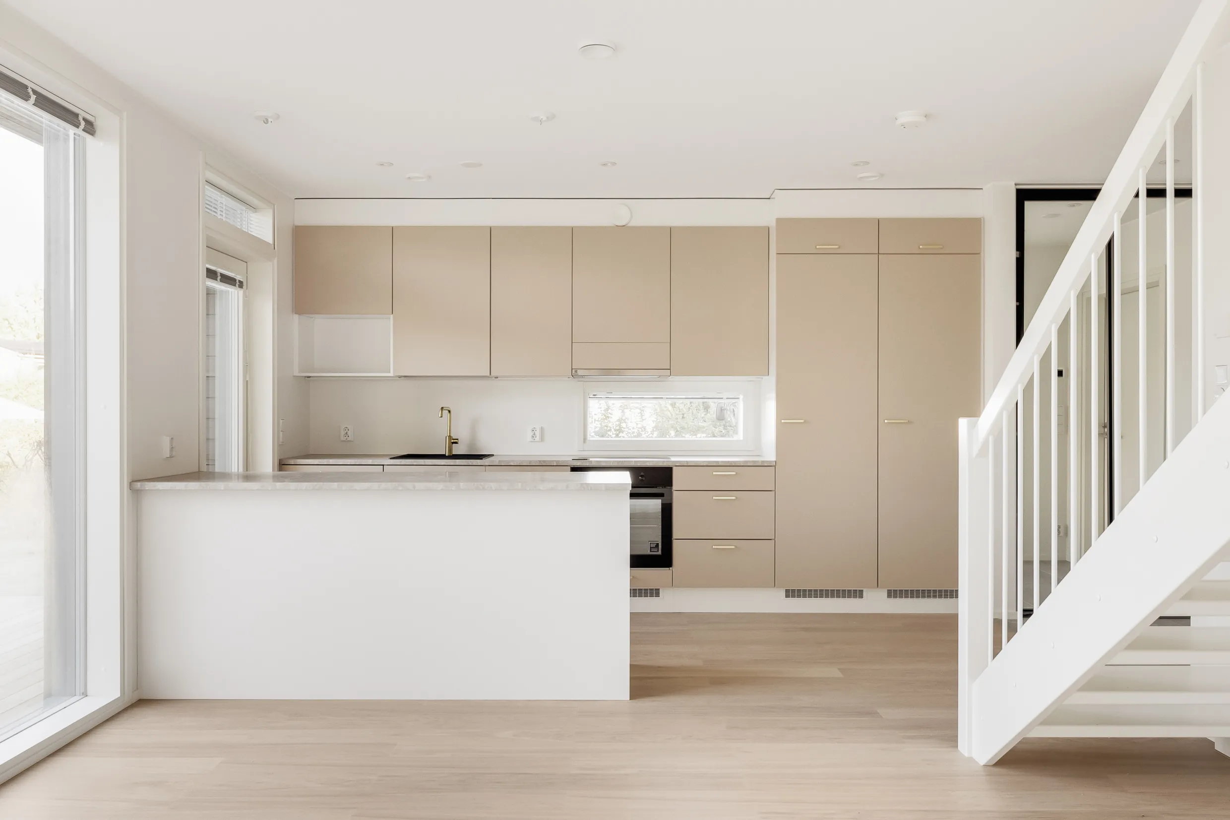 Vaalean keittiön ja valkoisten portaiden sisätila, jossa on puulattia ja luonnonvaloa.