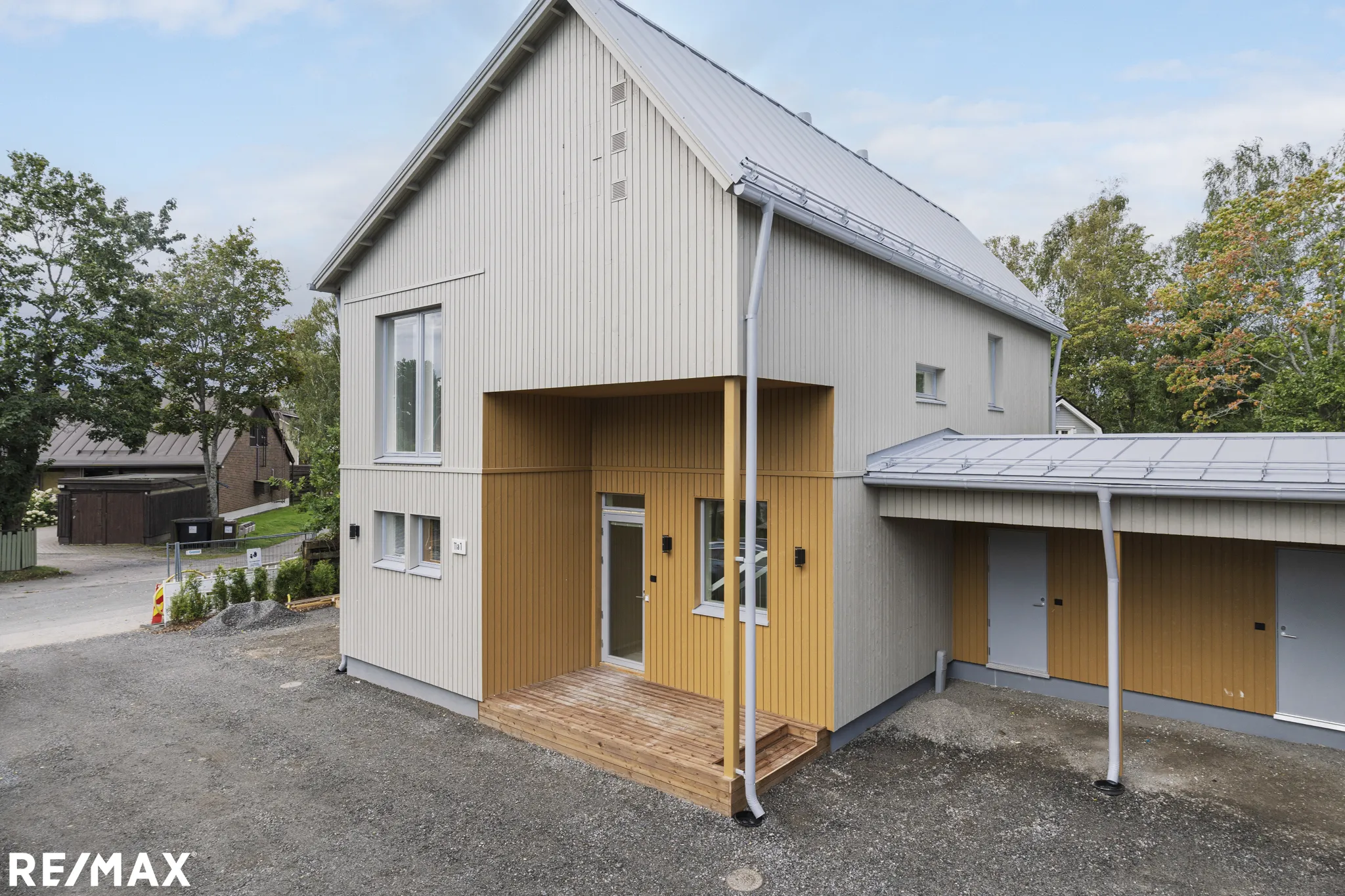 Moderni, kaksikerroksinen omakotitalo, jossa on harmaa ulkovuoraus ja puinen terassi, valoisa sää.