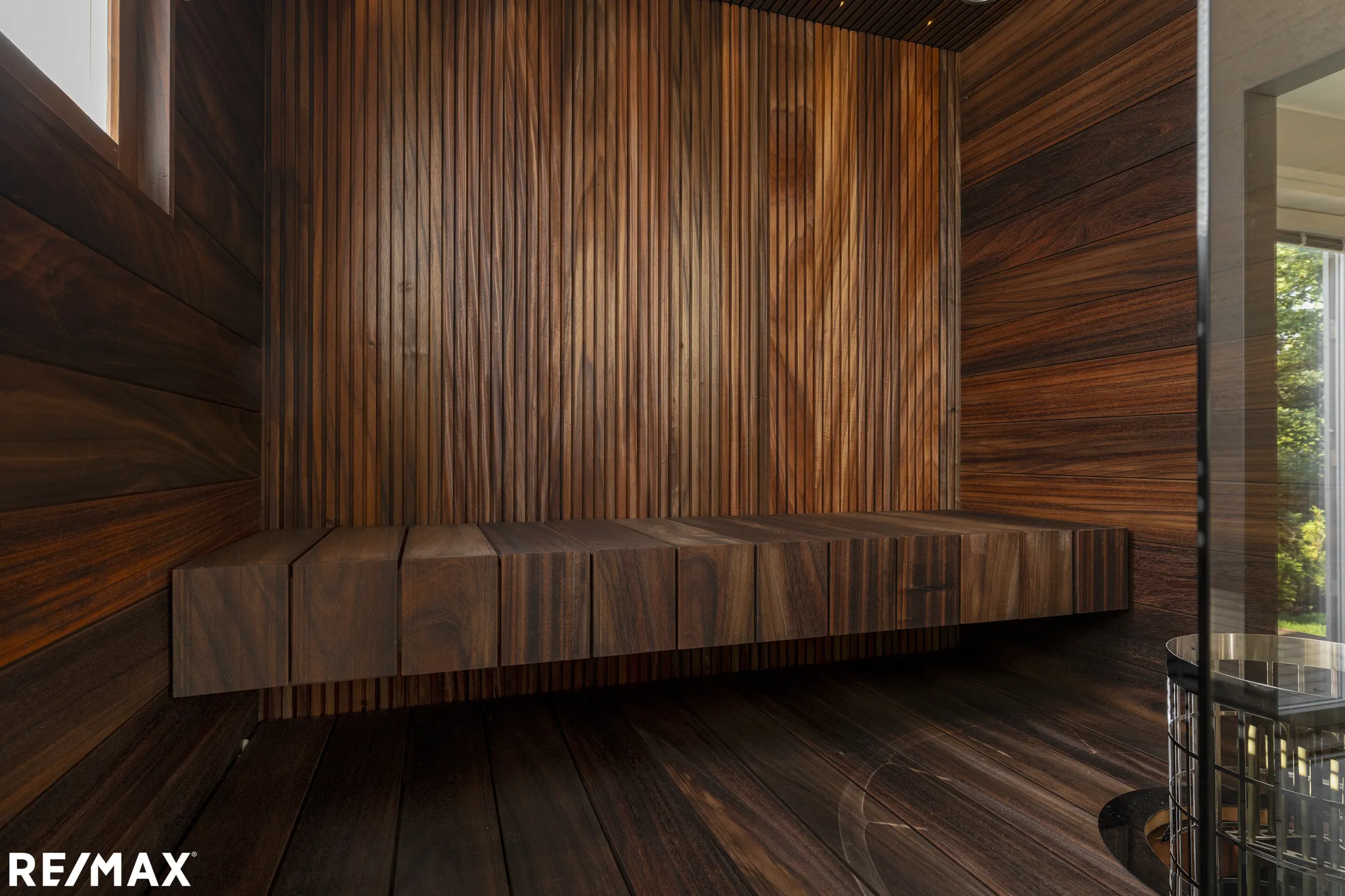 Puinen sauna, penkki ja RE/MAX-logo.
