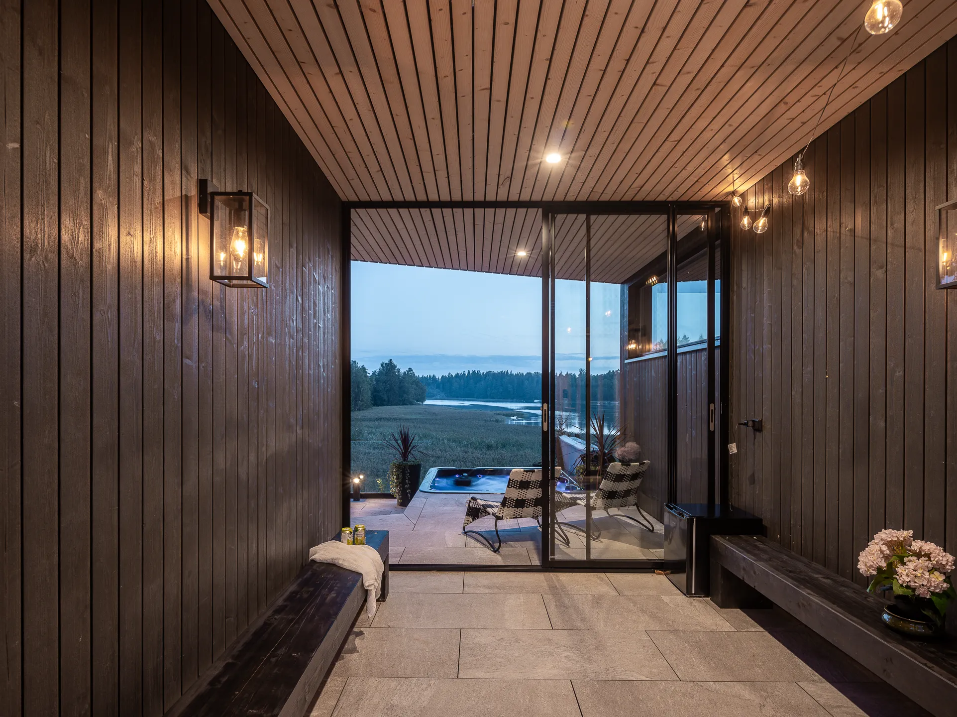 Sisätila, jossa on puupanelointi, liukuovet ulkotilaan, jossa on poreallas ja järvinäkymä, sekä tunnelmallinen valaistus.