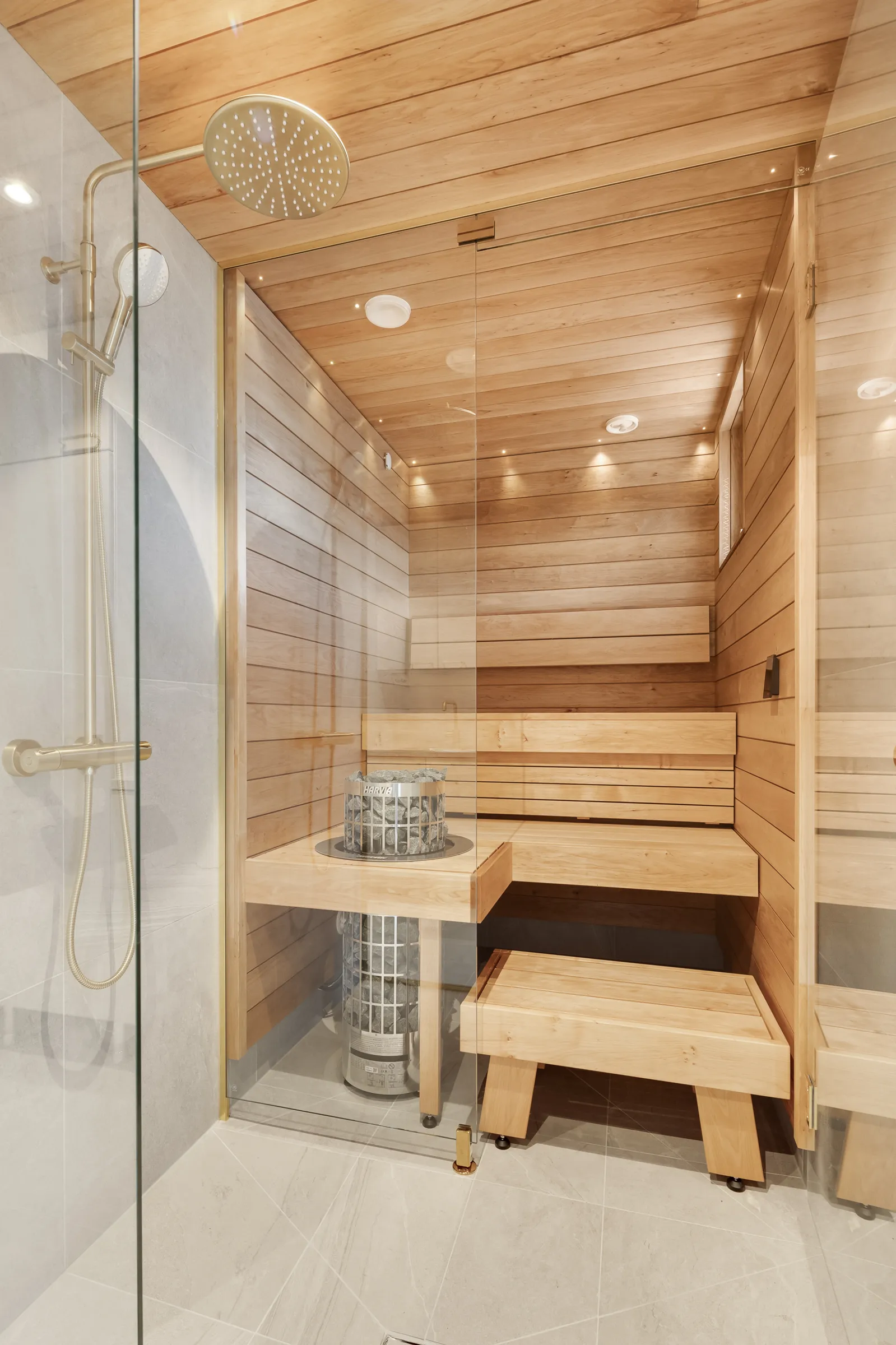 Moderni sauna lasiseinällä, puupaneeleilla ja metallisella kiukaalla sekä suihkulla.