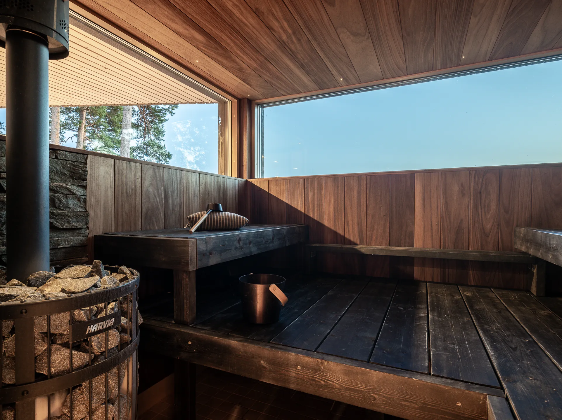 Sauna, jossa on puupanelointi, kivikiuas, puiset penkit ja ikkunat, joista näkyy ulos.