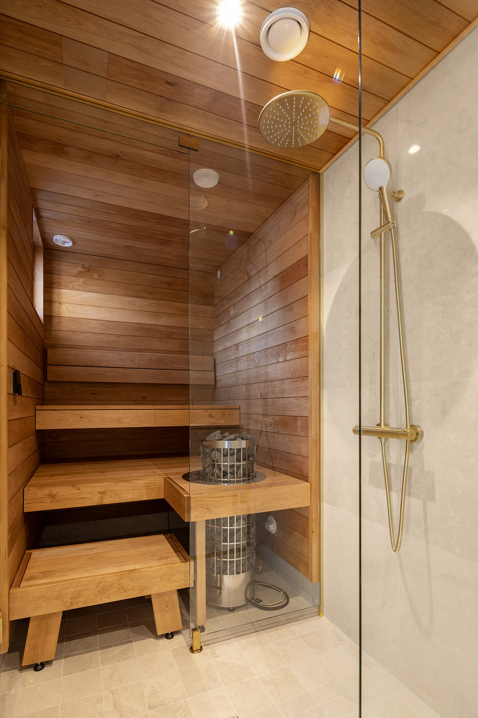 Sauna ja suihku, puupanelointi, kultainen suihku, kivikiuas, lämmin valaistus.