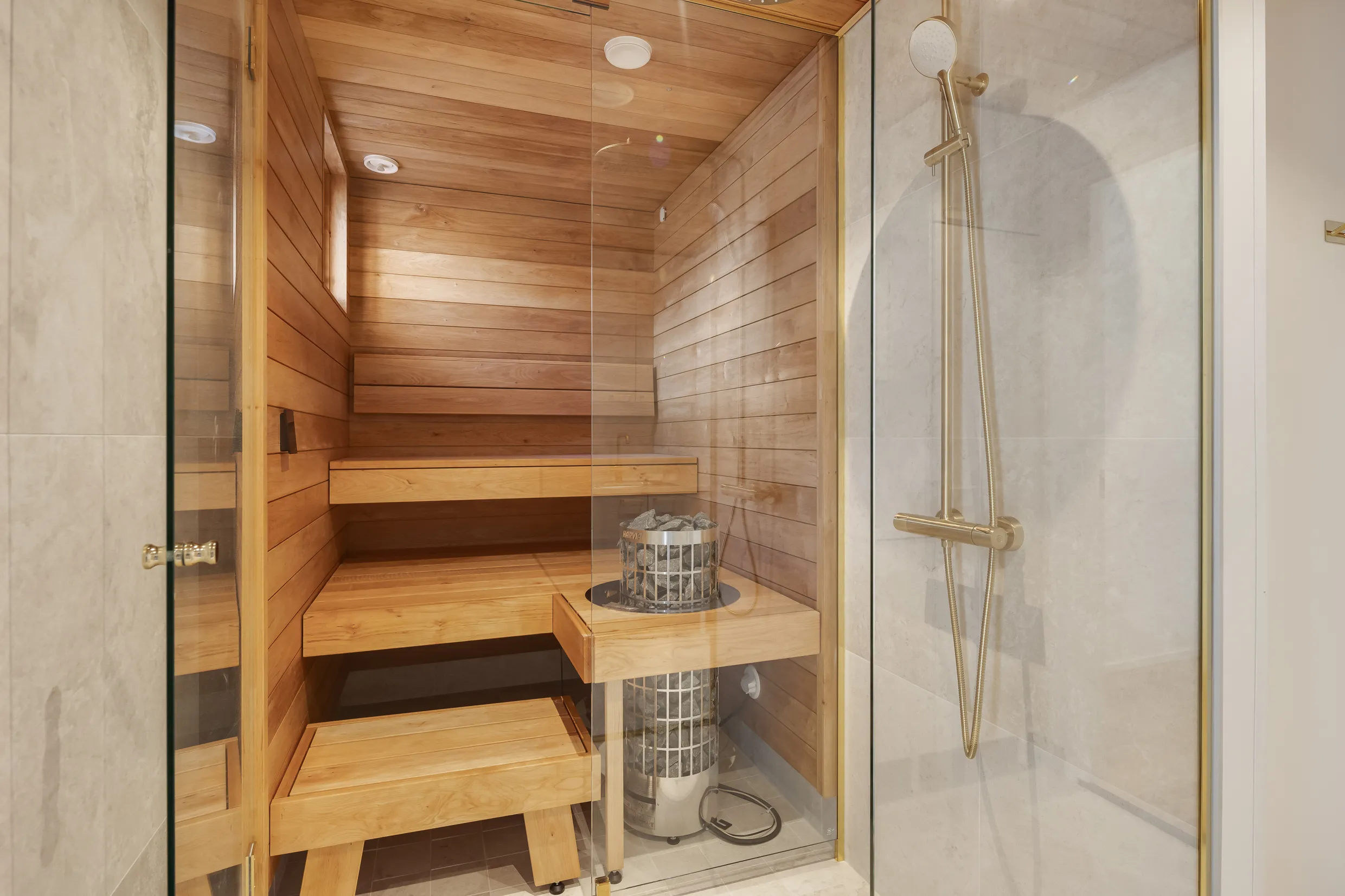 Saunan ja suihkun yhdistelmä, jossa on puupanelointi, kivikiuas ja kultainen suihku.