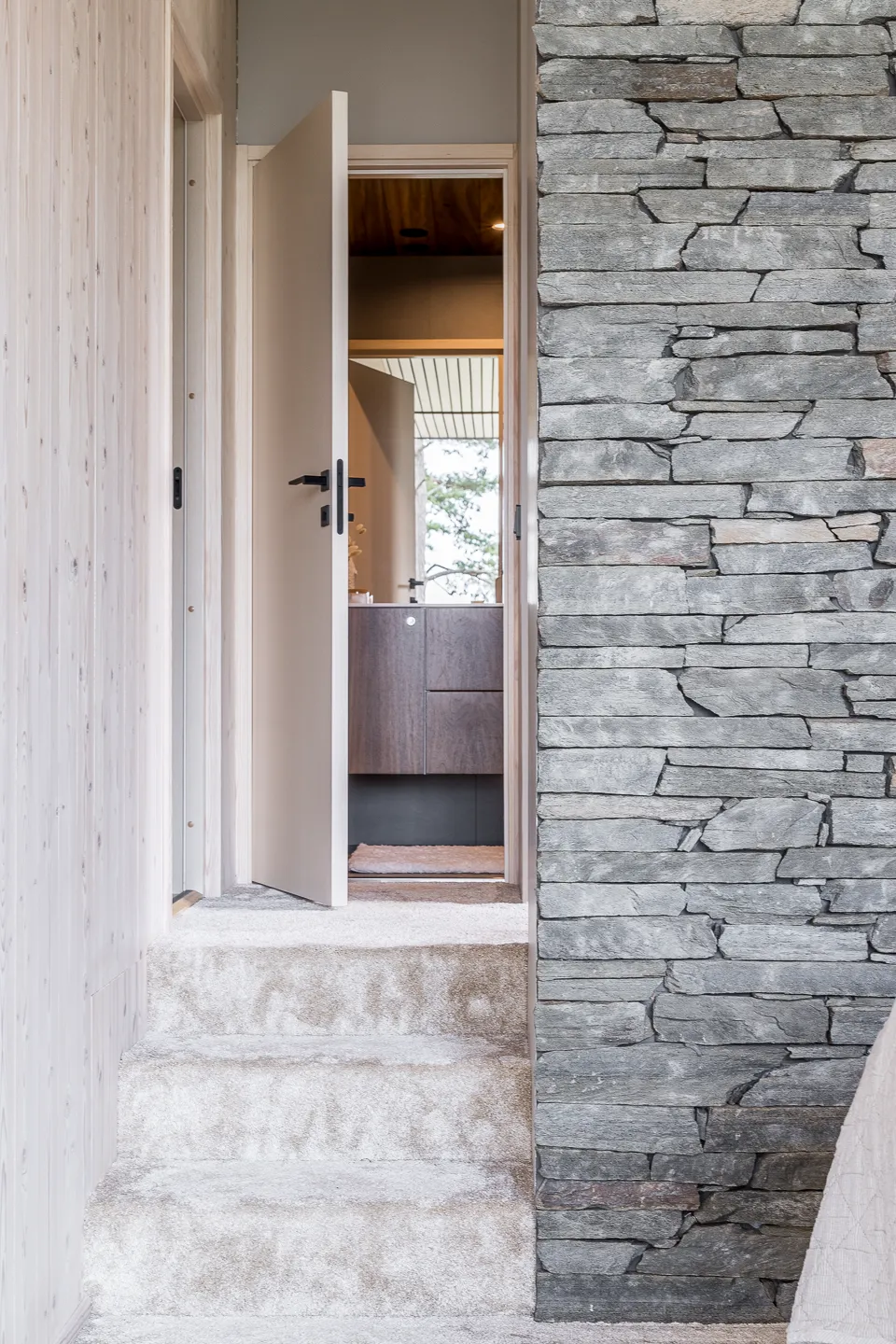 Sisätiloissa näkyy avoin ovi kylpyhuoneeseen, jossa on kiviseinä, puupanelointi ja matolla päällystetyt portaat. Kylpyhuoneessa on puinen pesuallas ja peili.