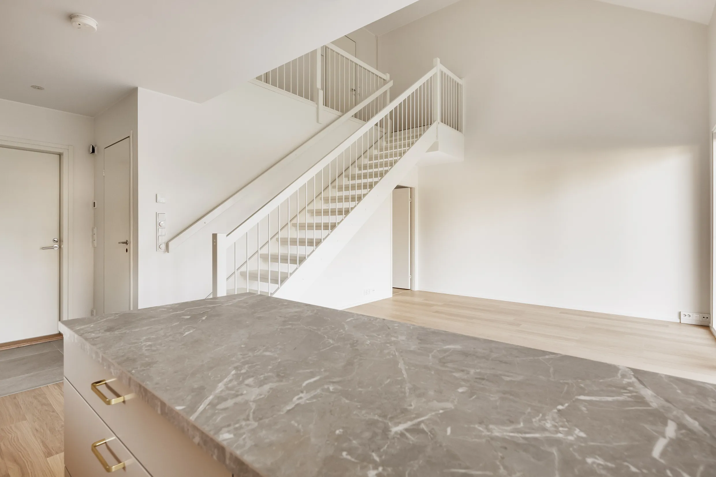 Vaaleanharmaa keittiösaareke, valkoiset portaat, valoisa huone.