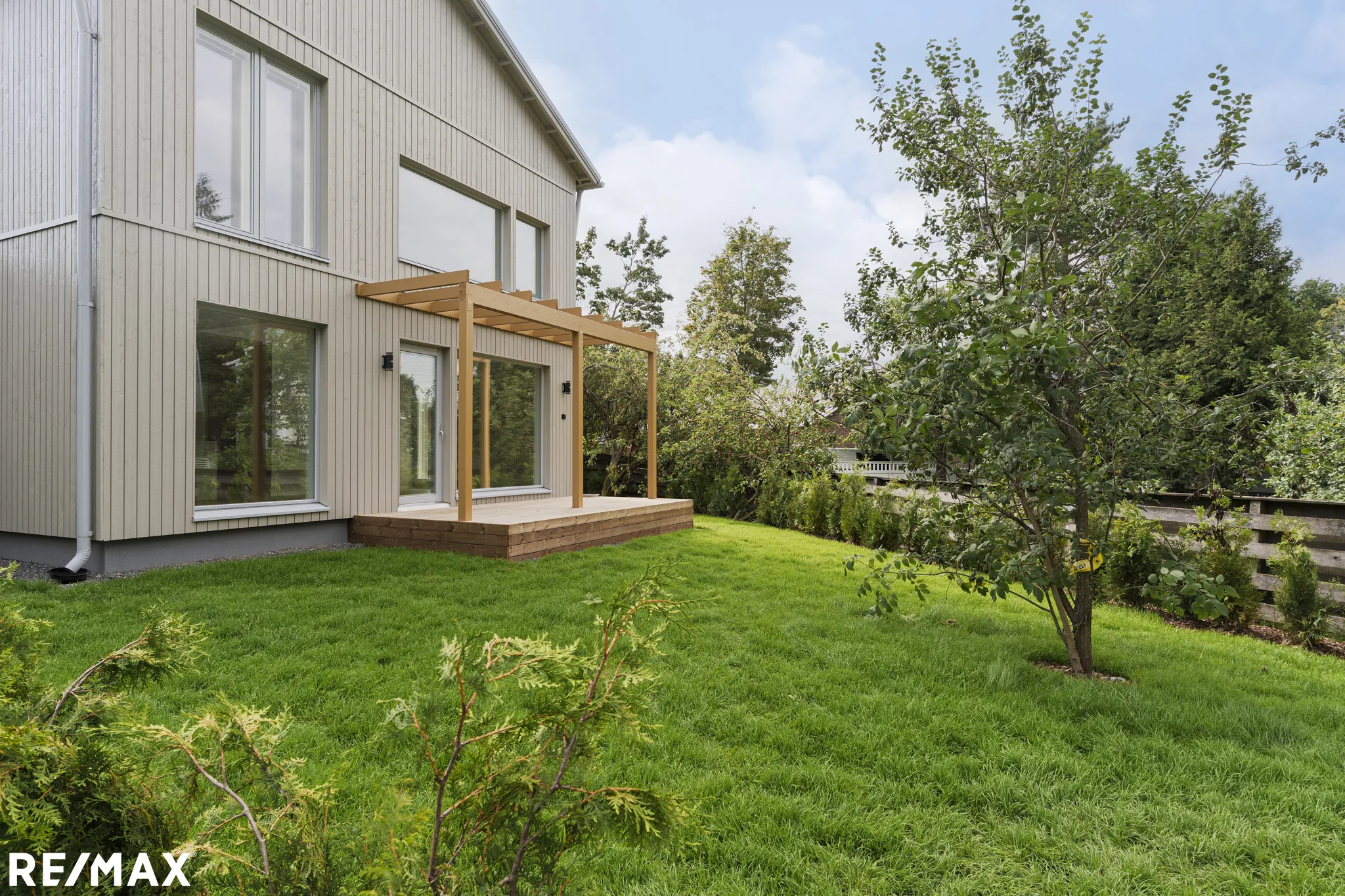 Moderni puutalo, vihreä nurmikko, aurinkoinen sää.