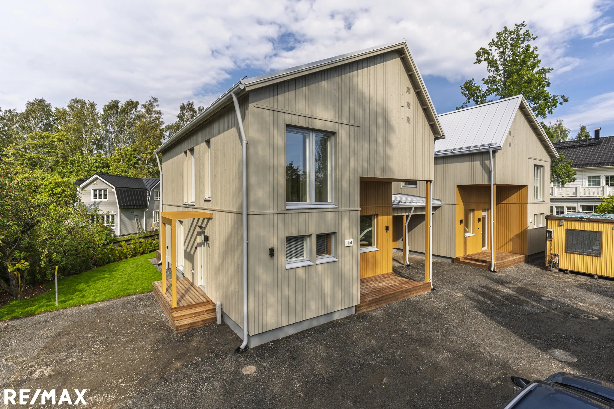 Kaksi modernia puutaloa harmaalla ja keltaisella värityksellä, aurinkoinen sää.