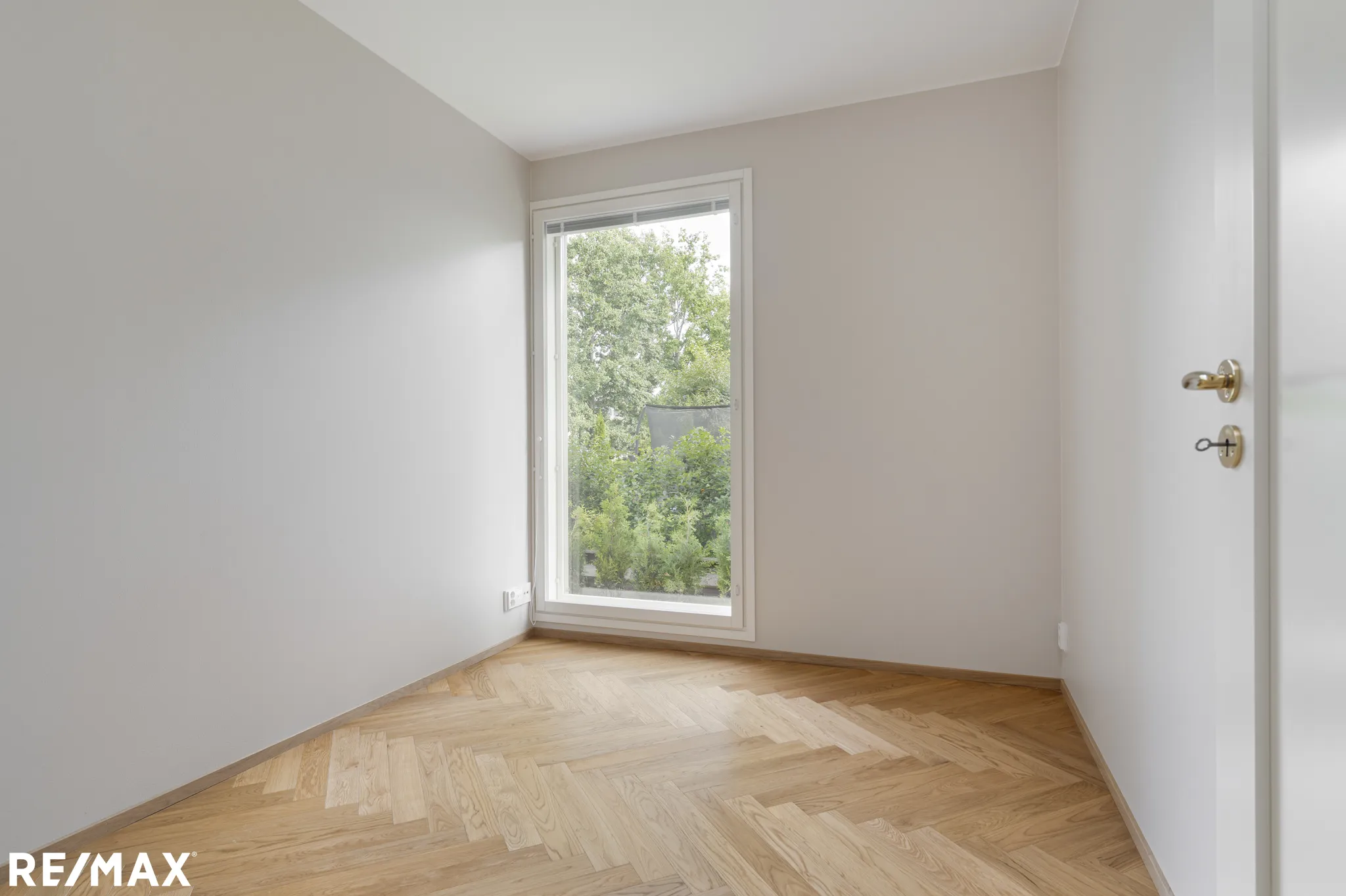 Valoisa huone, jossa on parkettilattia, suuri ikkuna ja valkoiset seinät.