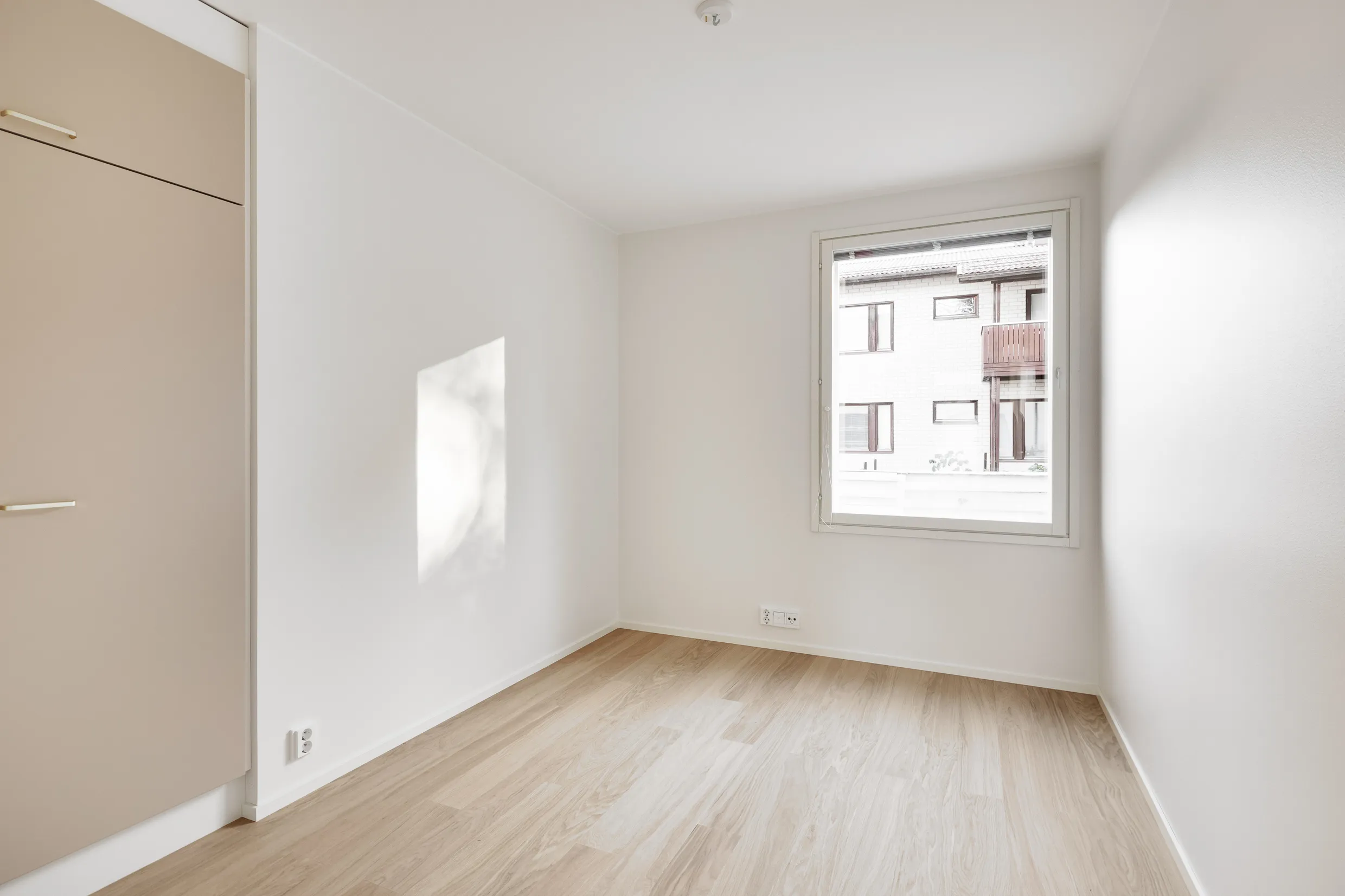 Vaalea huone, jossa on vaaleat puulattiat, valkoinen seinä ja ikkuna. Vaatekaappi vasemmalla.