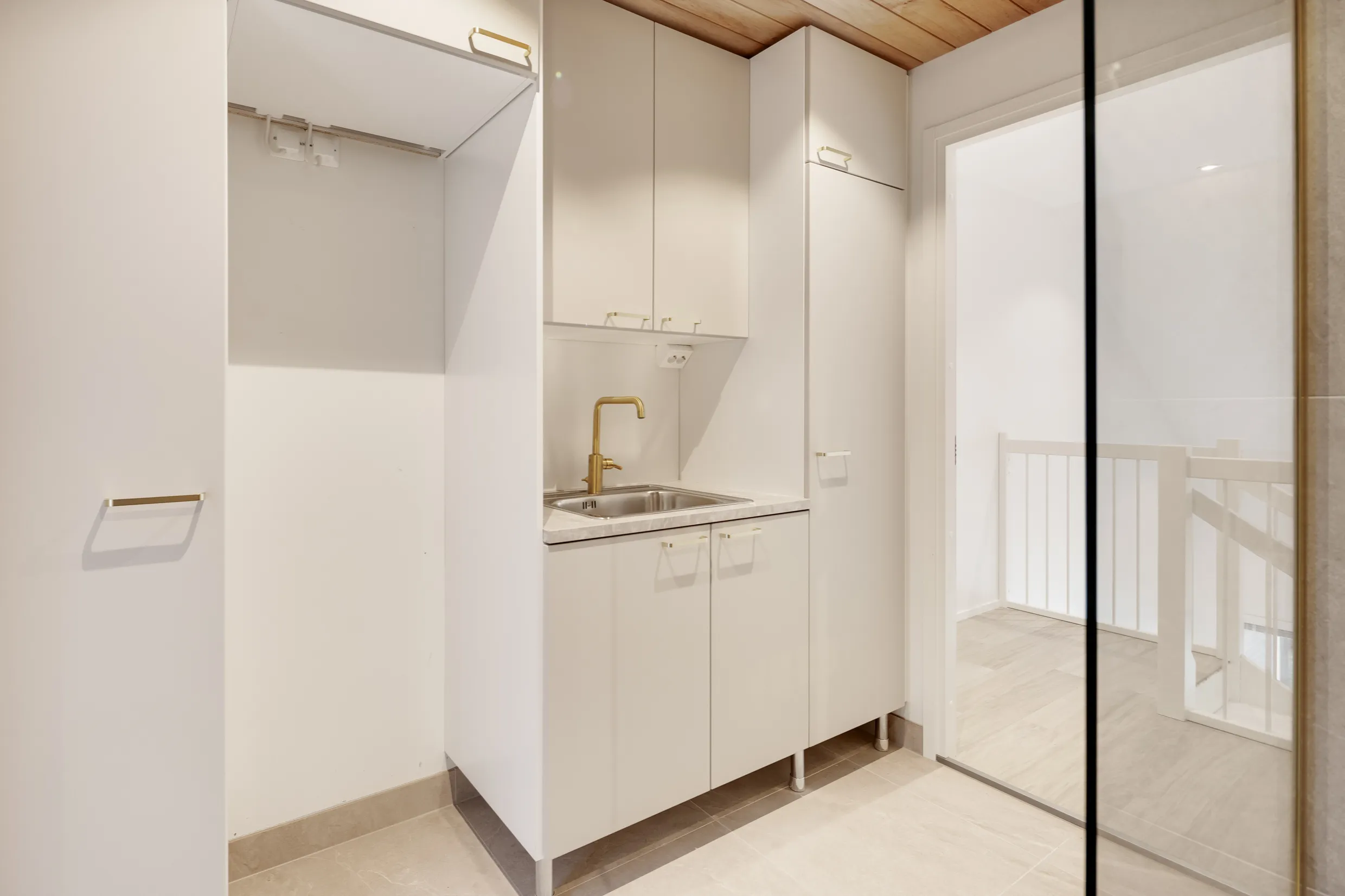 Vaaleassa huoneessa on valkoiset kaapit, kultainen hana ja peili, jossa näkyy portaikko.