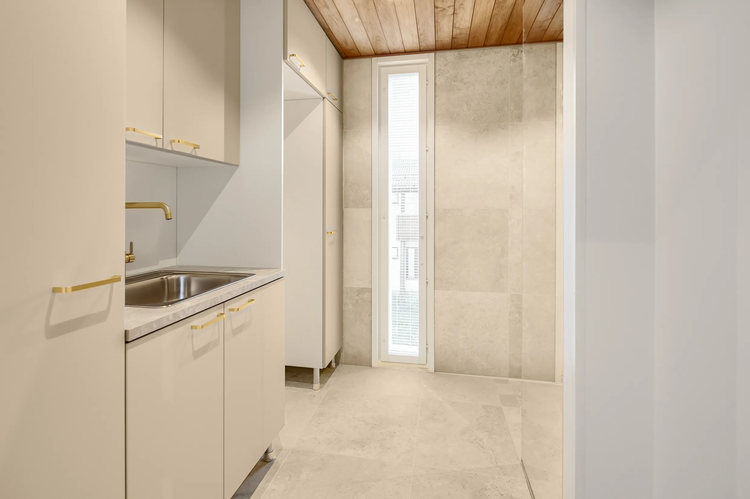 Vaalean huoneen pesuallas, kaapit, puukatto ja ikkuna, jossa on sälekaihtimet.