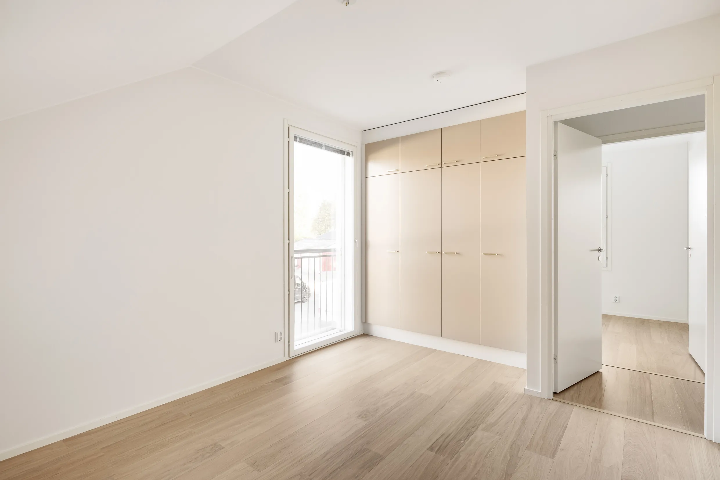 Vaalea huone, jossa on vaaleat puulattiat, valkoiset seinät, vaatekaappi ja parvekeovi.