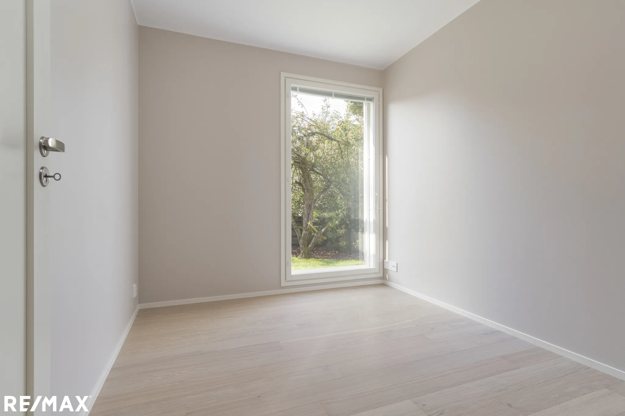 Vaalea huone, ikkuna ja RE/MAX-logo.