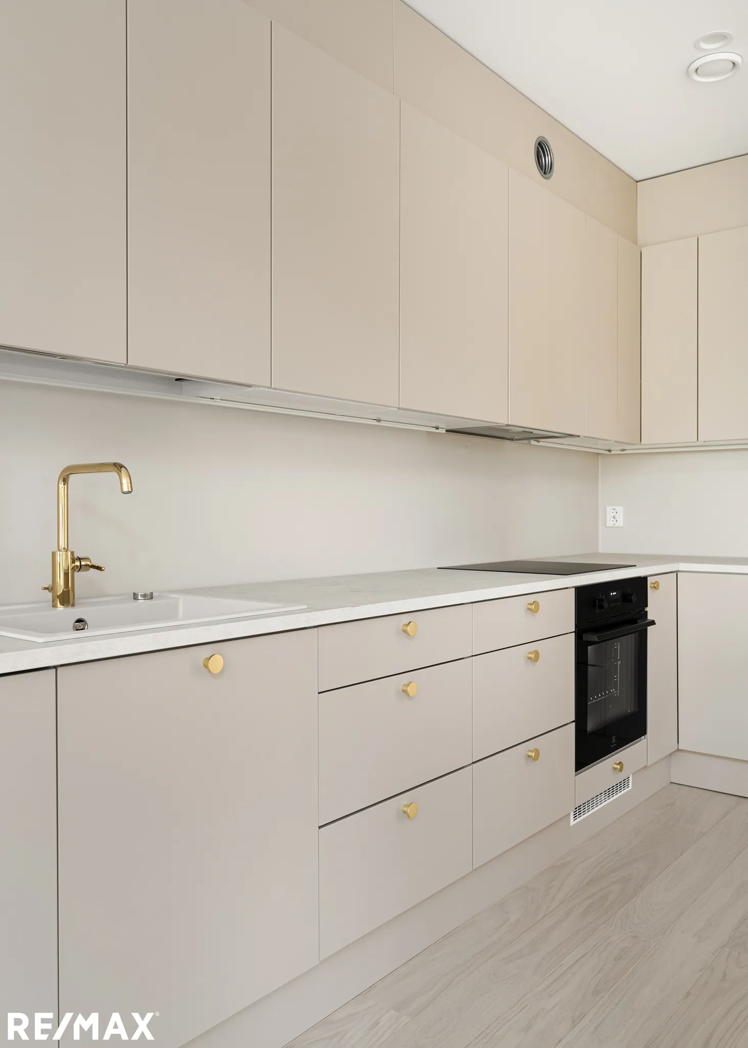 Vaalean keittiönäkymä, kultaiset hanat, moderni uuni, RE/MAX-logo alhaalla.