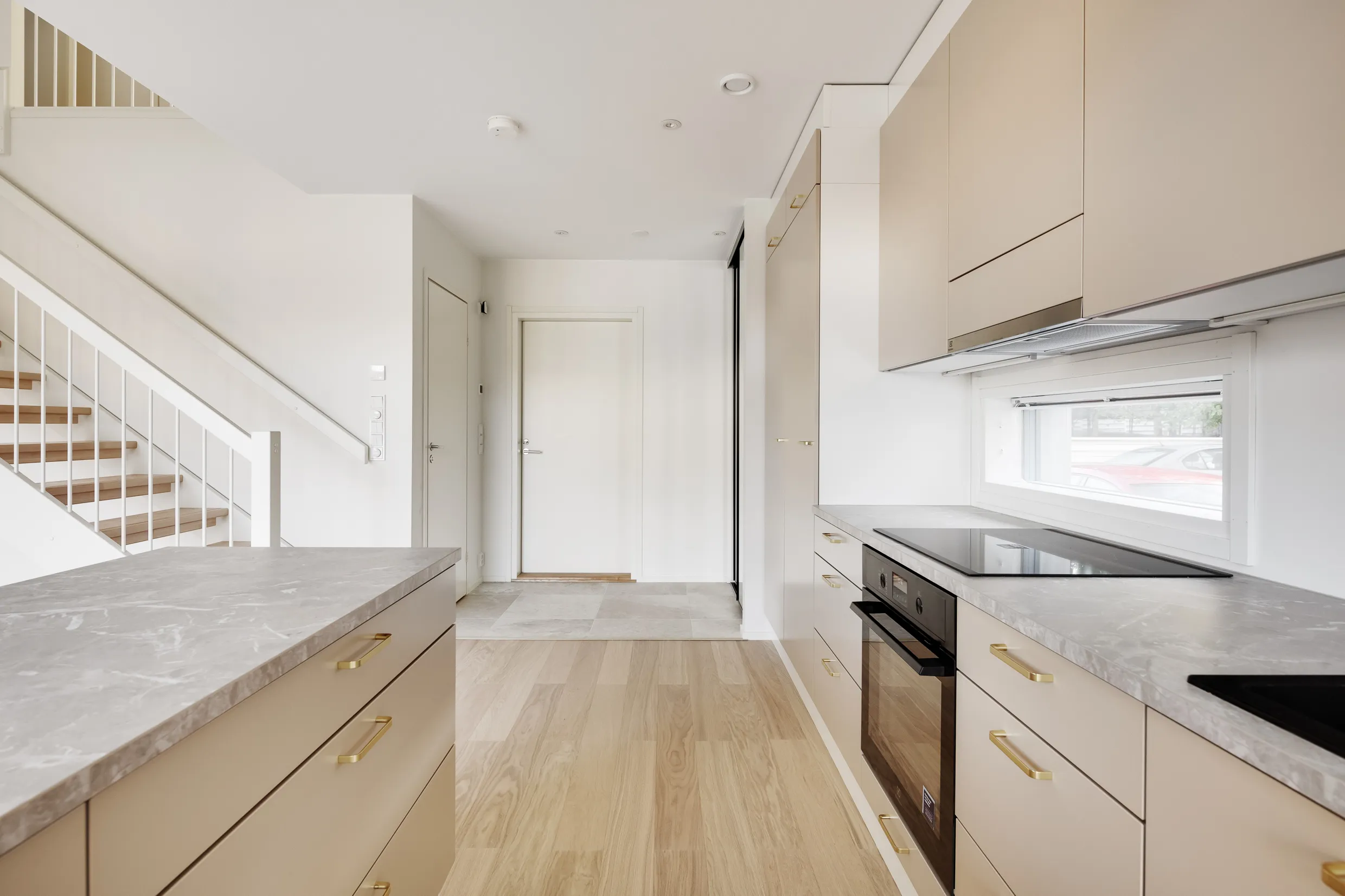 Vaalean keittiön sisustus, jossa on marmoritasot, kultaiset vetimet ja puuportaat. Valoisa ja moderni tunnelma.