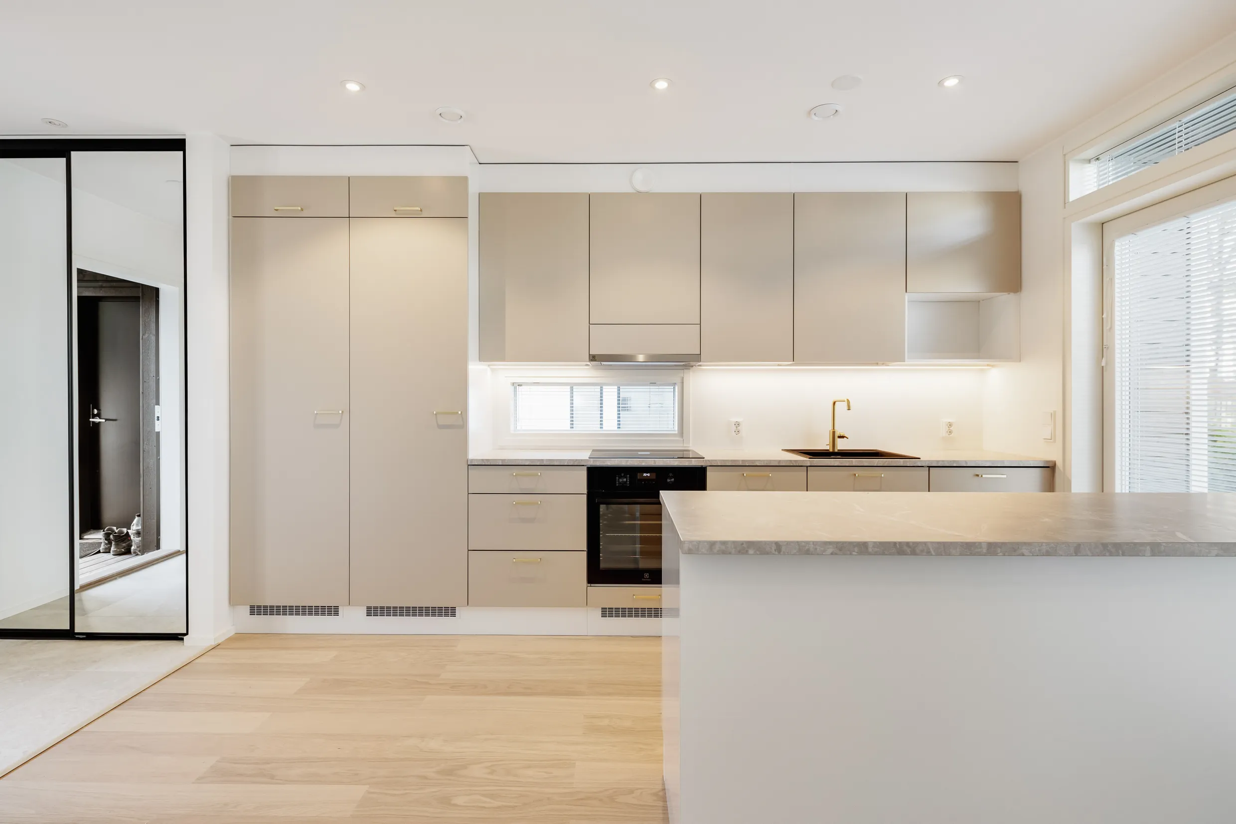 Vaalean keittiön sisustus saarekkeella, puulattialla ja modernilla valaistuksella.