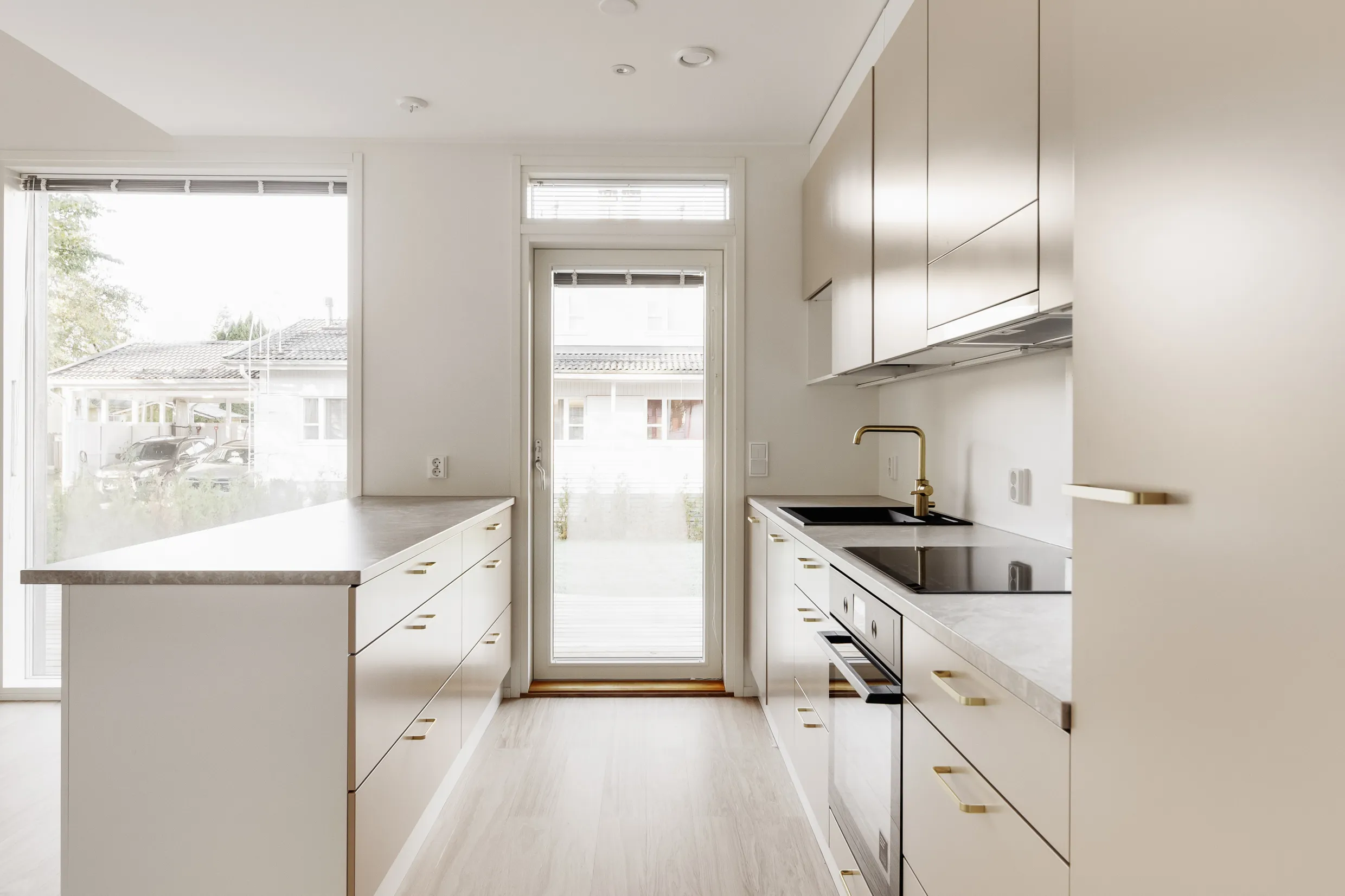 Vaaleassa keittiössä on valkoiset kaapit, kultaiset vetimet, marmorinen työtaso ja suuri ikkuna, josta näkyy ulos.