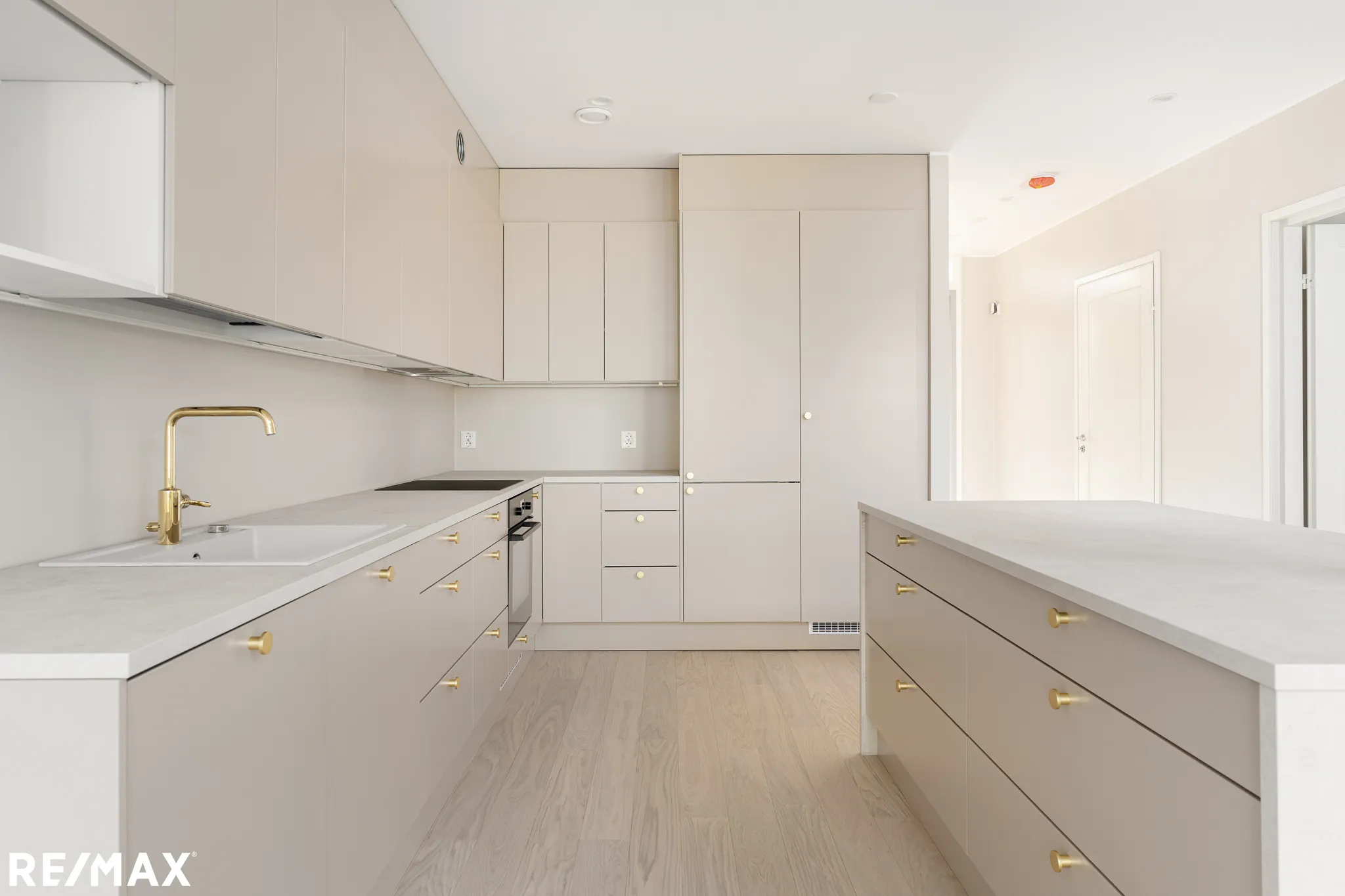 Vaalean keittiön sisustus kultaisilla yksityiskohdilla, saareke ja puulattia.