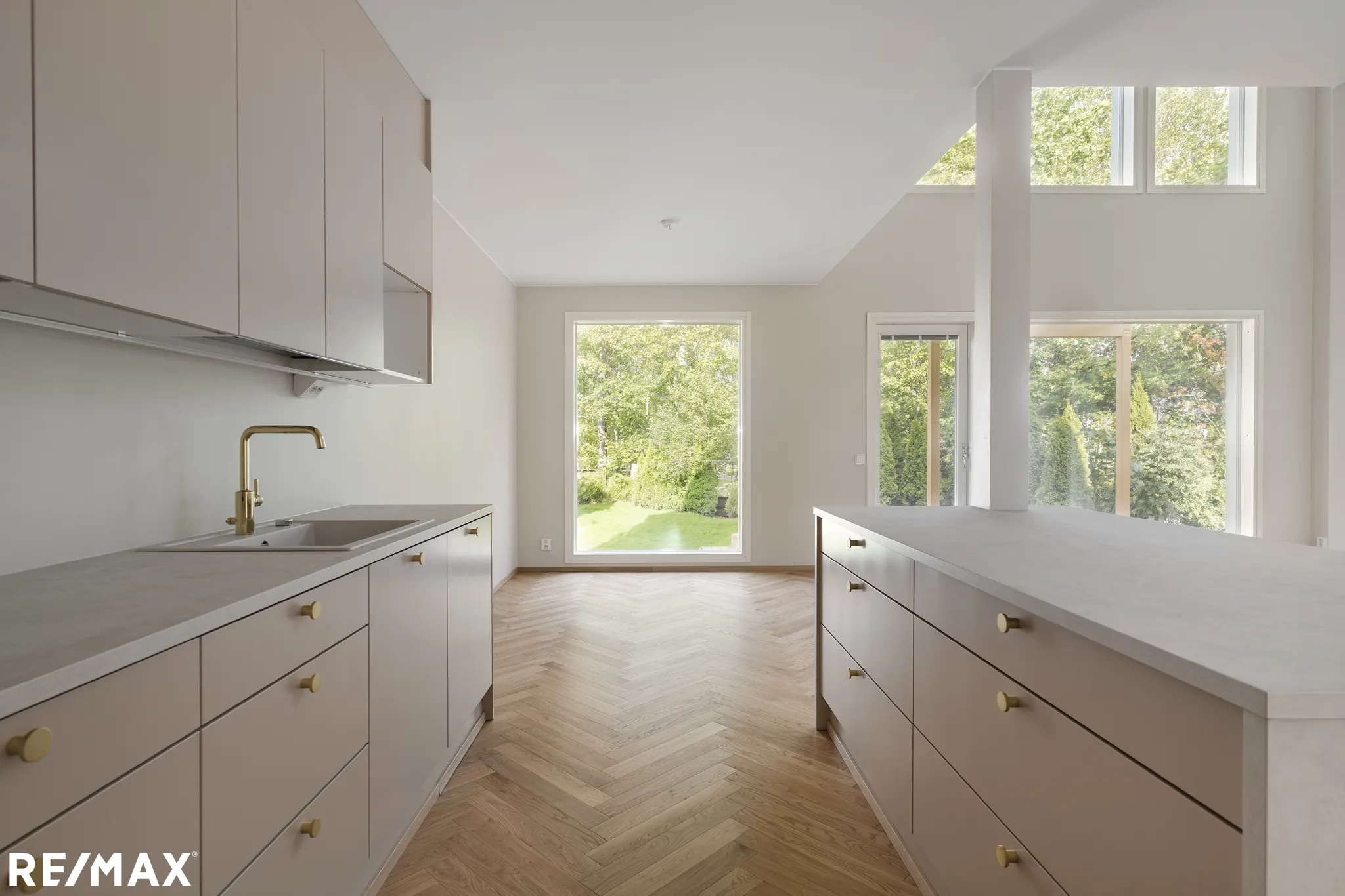 Vaaleassa keittiössä on vaaleat kaapit, kultaiset hanat ja parkettilattia kalanruotokuviolla. Suuret ikkunat tuovat luonnonvaloa.