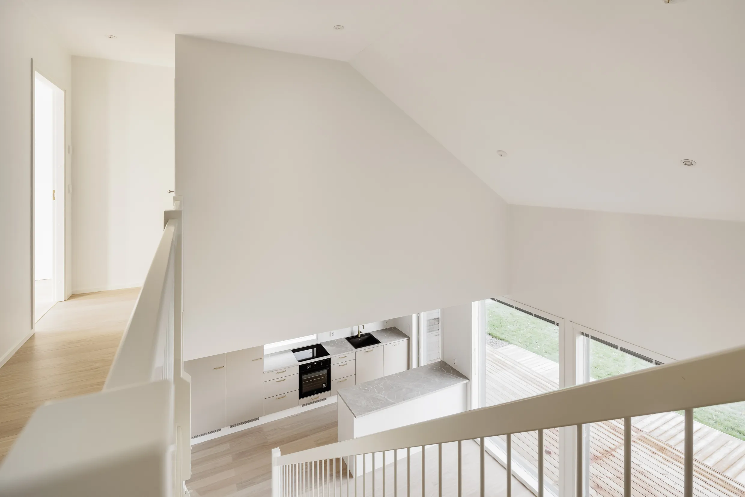 Valoisa ja moderni sisätila, jossa näkyy portaikko, keittiö ja suuret ikkunat, kaikki valkoisena.