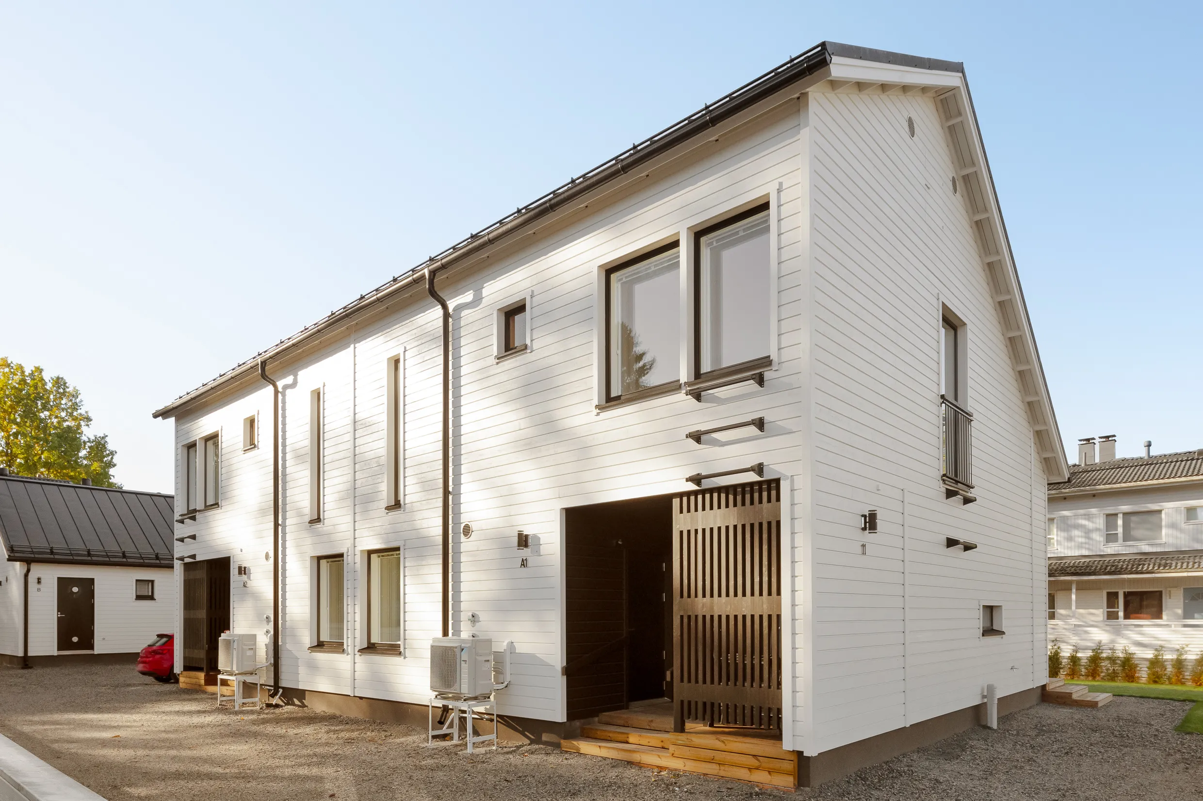 Moderni, valkoinen puutalo, jossa on tummat ikkunankarmit ja tumma katto, aurinkoisessa säässä.