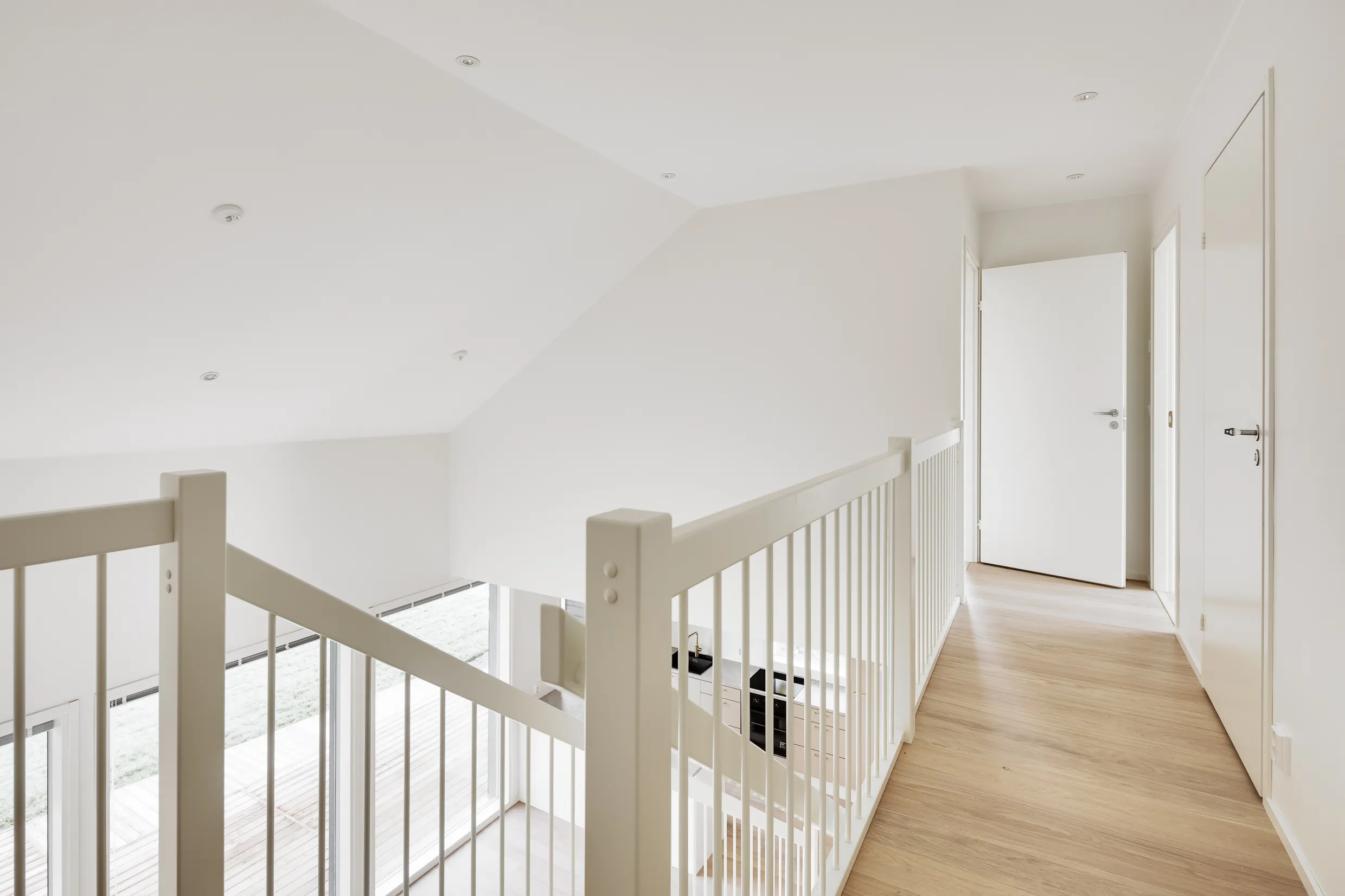 Vaalea, moderni sisätila, jossa valkoiset seinät, puinen lattia ja valkoinen portaikko.