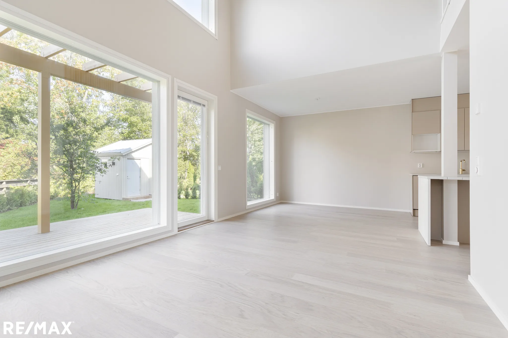 Vaalea, avara huone, jossa suuret ikkunat ja moderni keittiö.