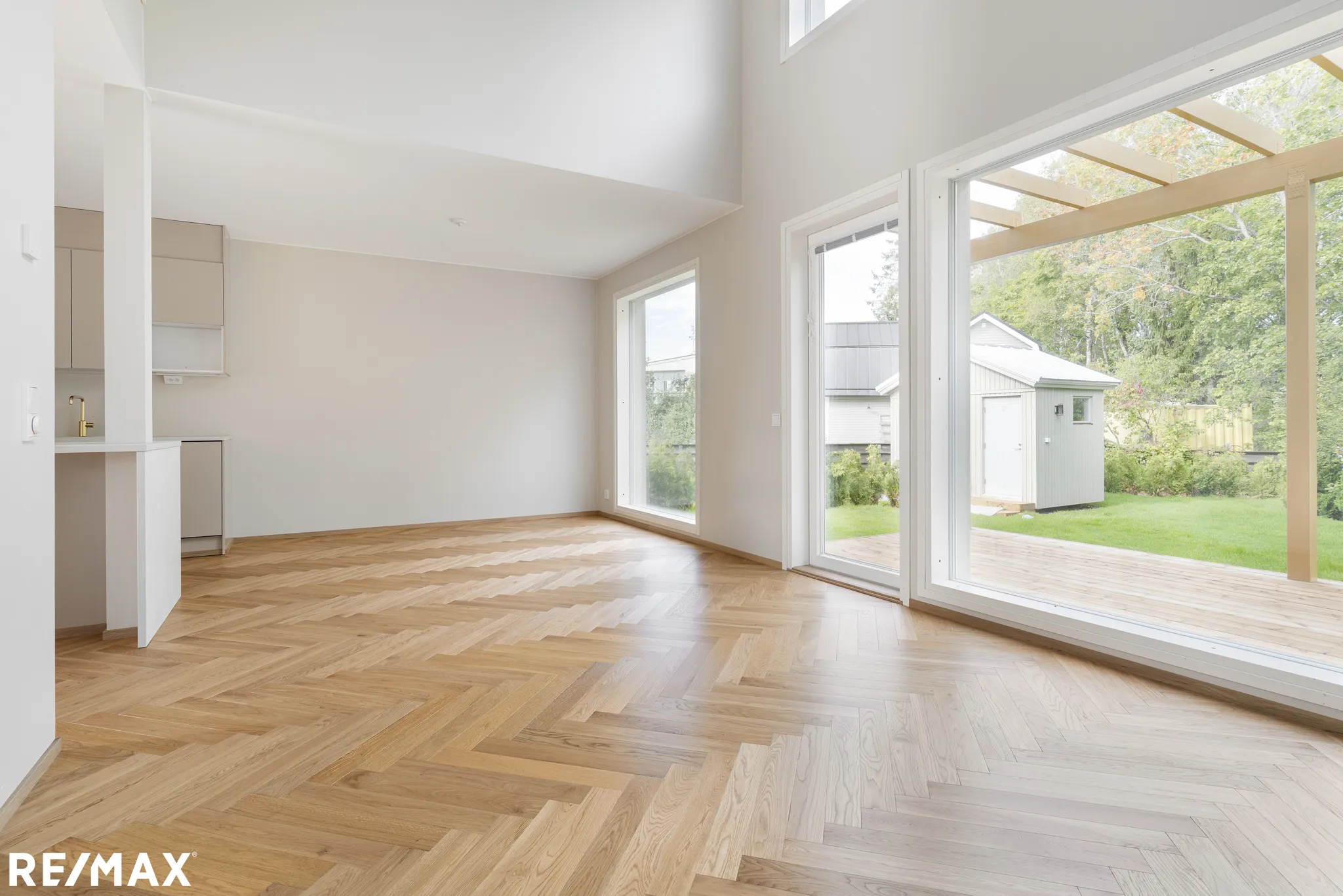 Valoisa huone parkettilattialla, suuret ikkunat ja näkymä ulos. Vaaleat seinät ja moderni keittiönurkkaus.