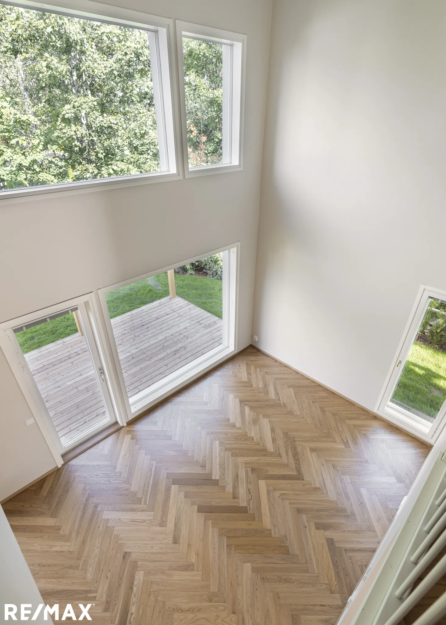 Korkeasta kuvakulmasta otettu kuva valoisasta huoneesta, jossa on parkettilattia, suuret ikkunat ja valkoiset seinät.