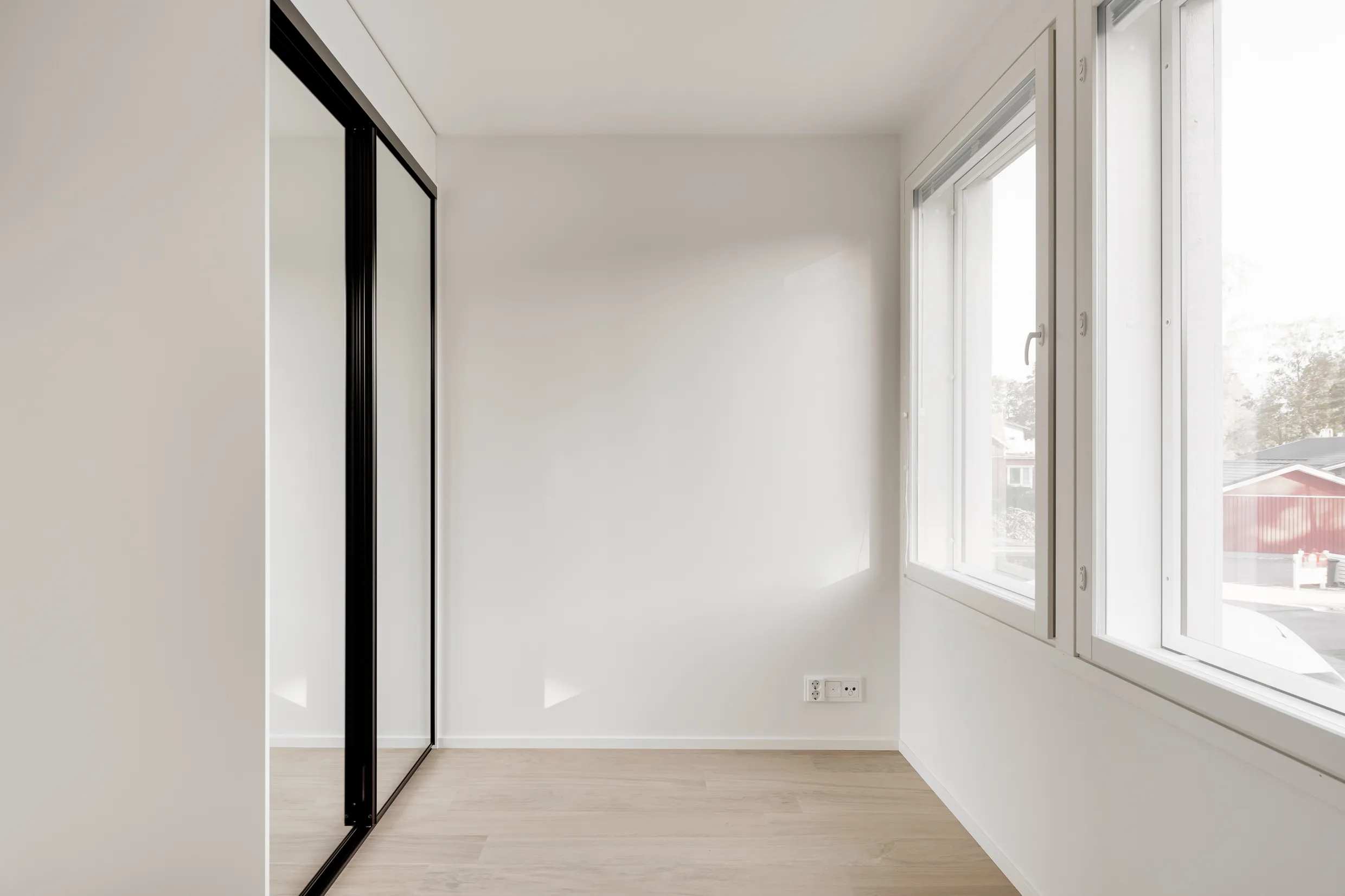 Vaalea huone, jossa on peililiukuovi, valkoiset seinät, vaalea puulattia ja ikkuna, josta näkyy ulos.