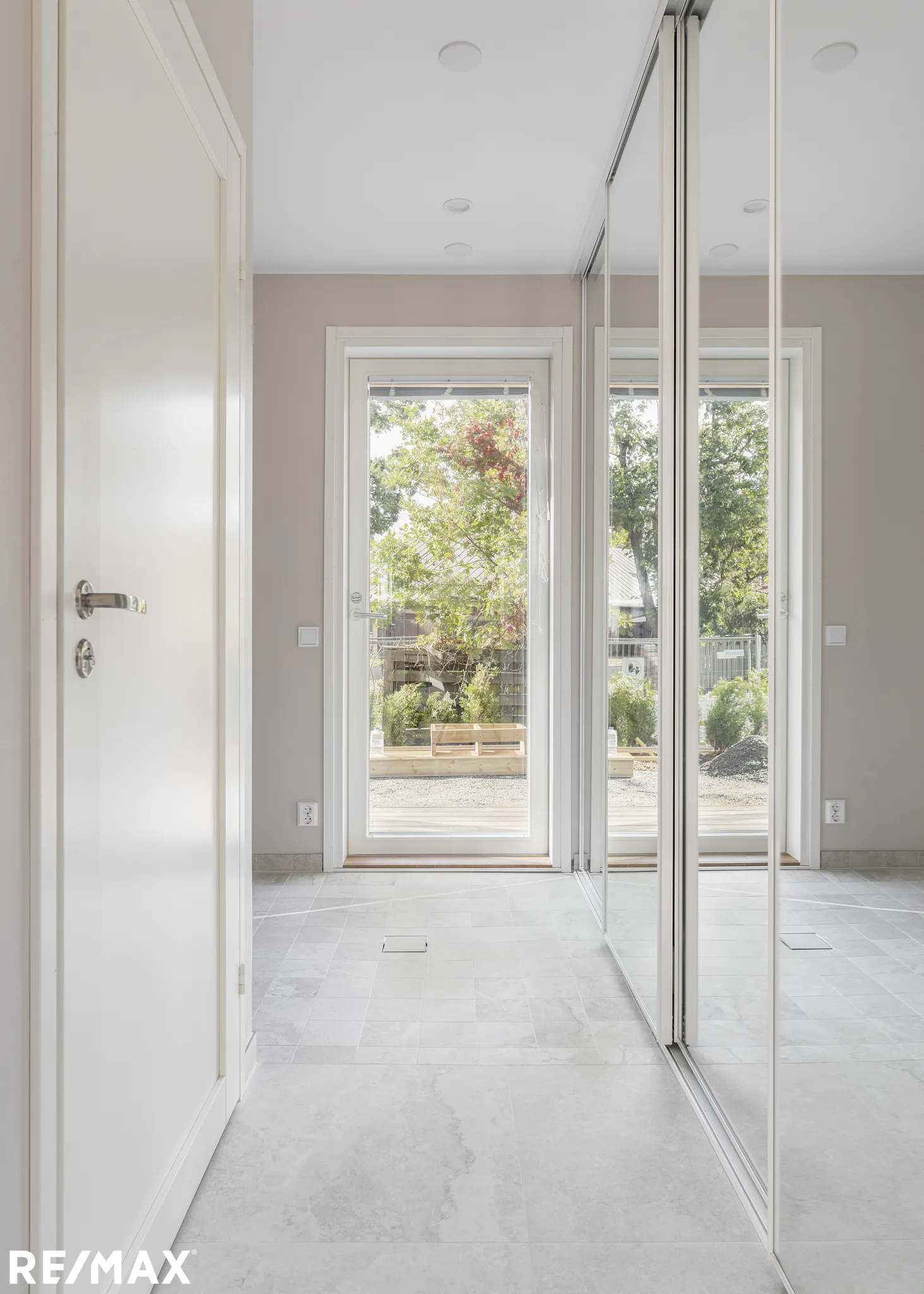 Vaalean huoneen sisustus, jossa valkoinen ovi, peililiukuovet ja näkymä ulos.