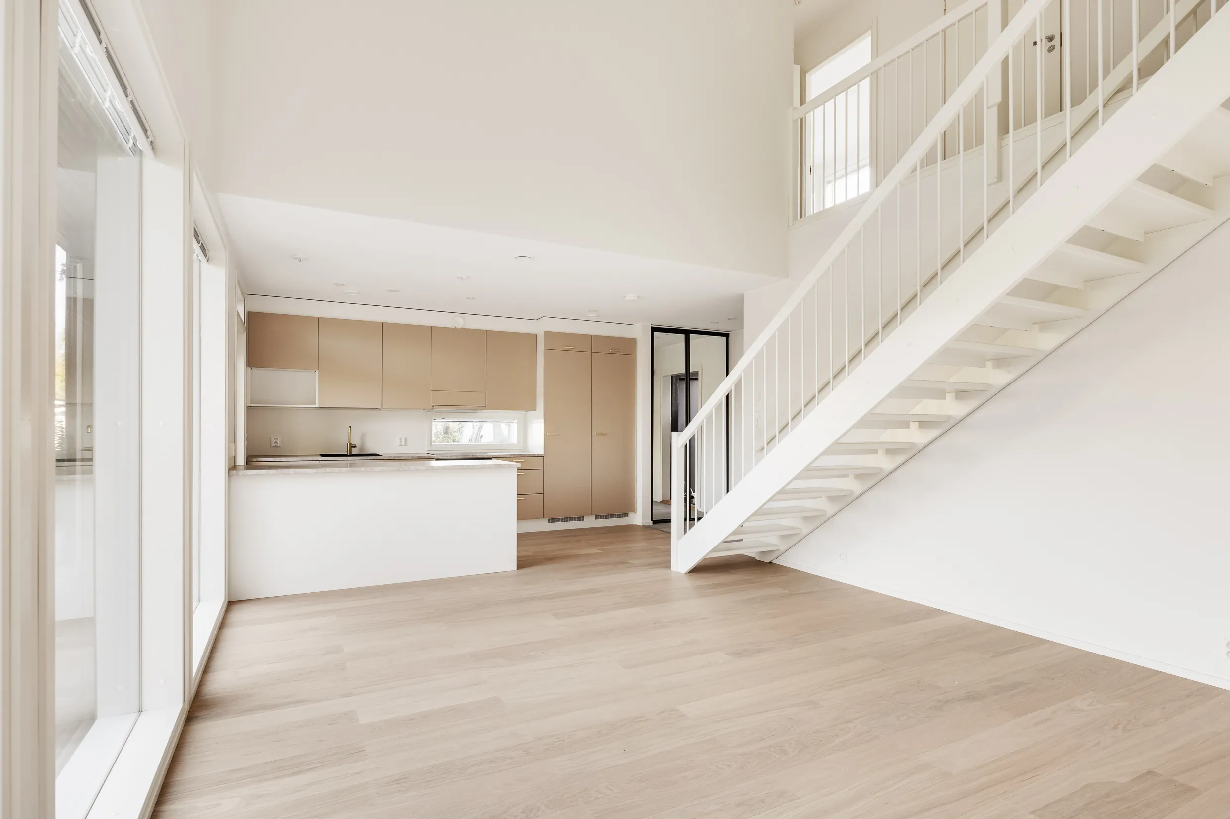 Vaalea, avara huoneisto, jossa on valkoinen portaikko, vaaleat puulattiat ja moderni keittiö.