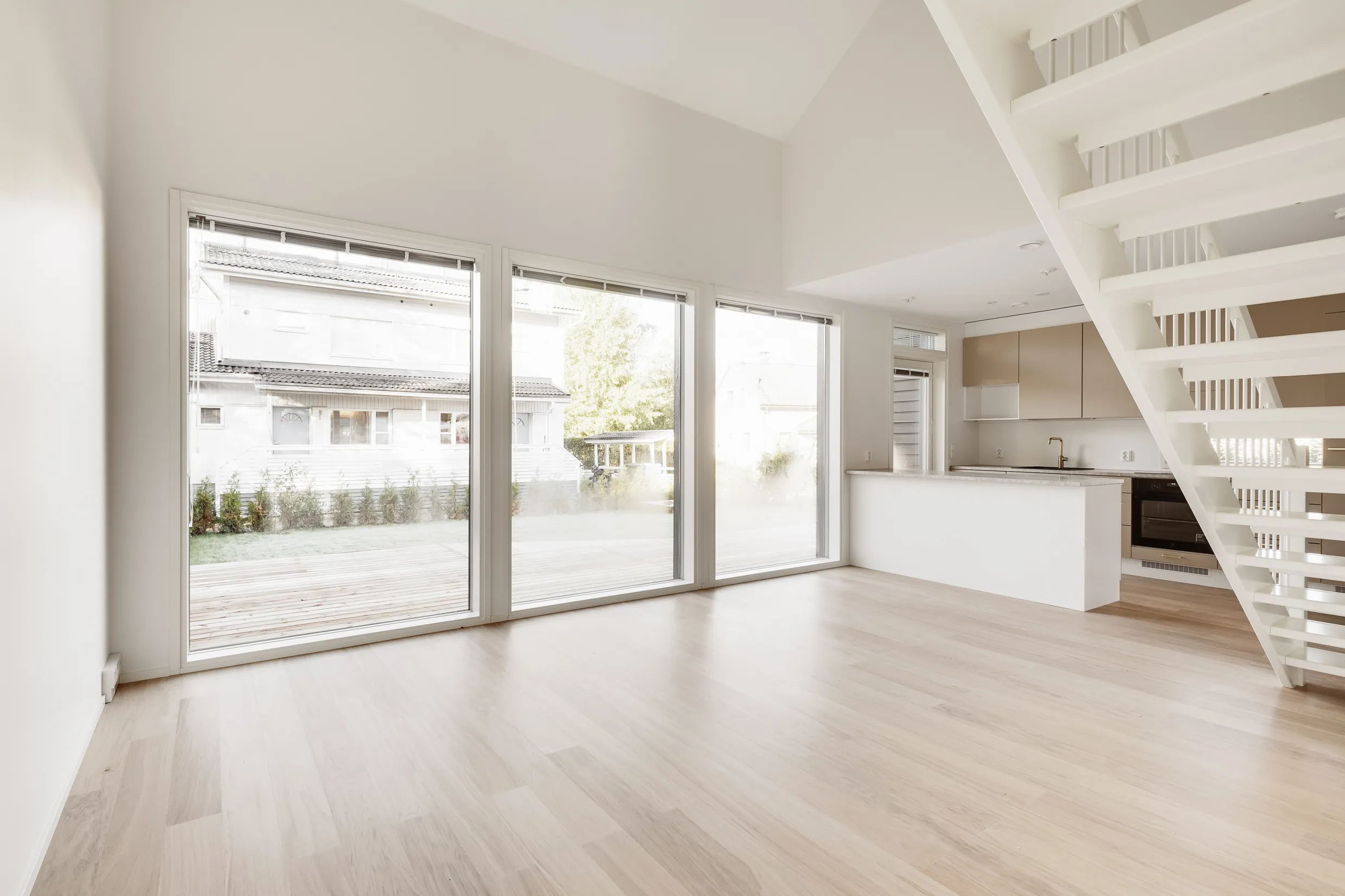Vaalea, avara huoneisto, jossa suuret ikkunat, valkoiset portaat ja moderni keittiö.
