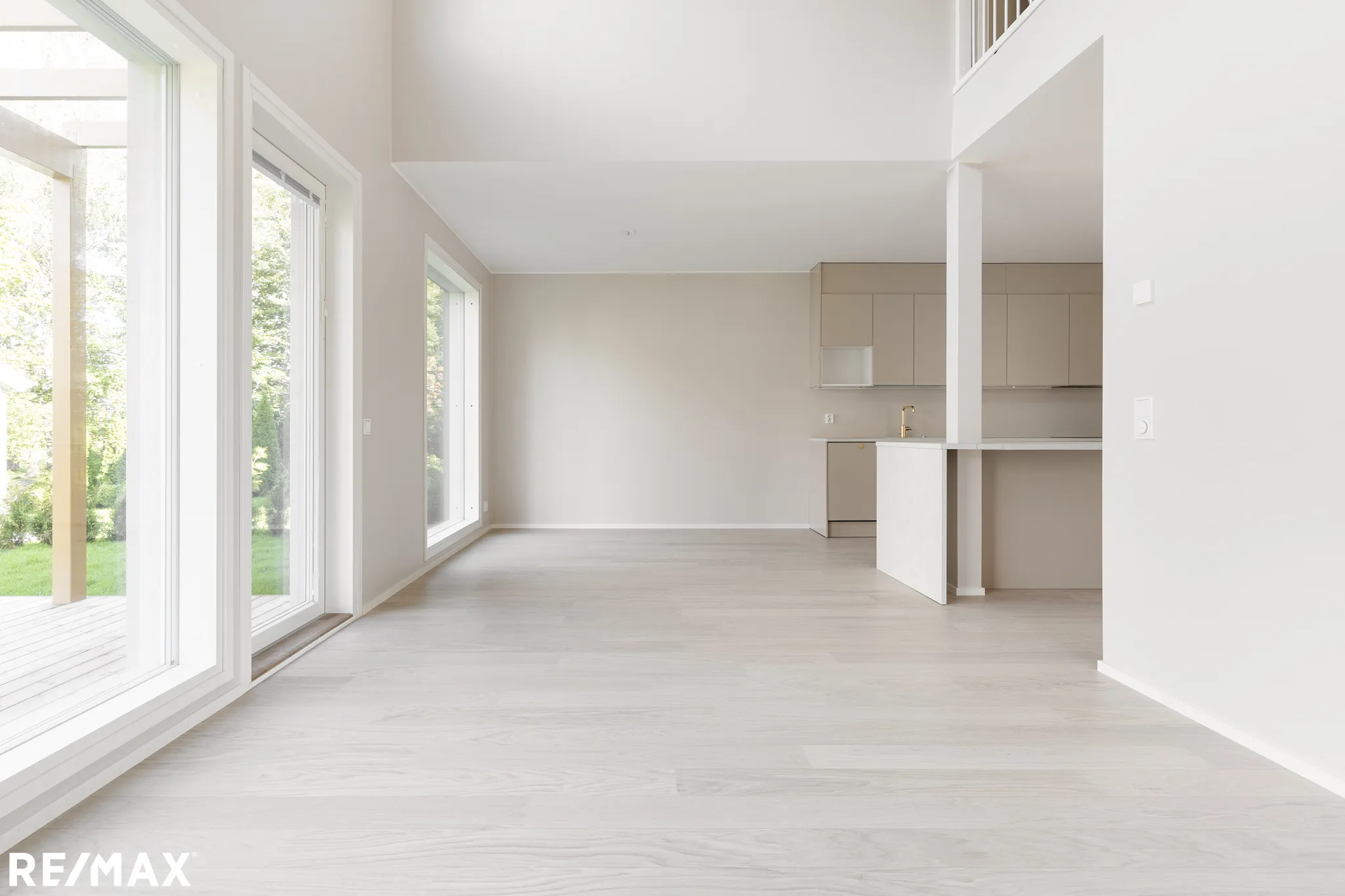 Vaalea ja avara huoneisto, jossa suuret ikkunat, vaaleat puulattiat ja moderni keittiö.