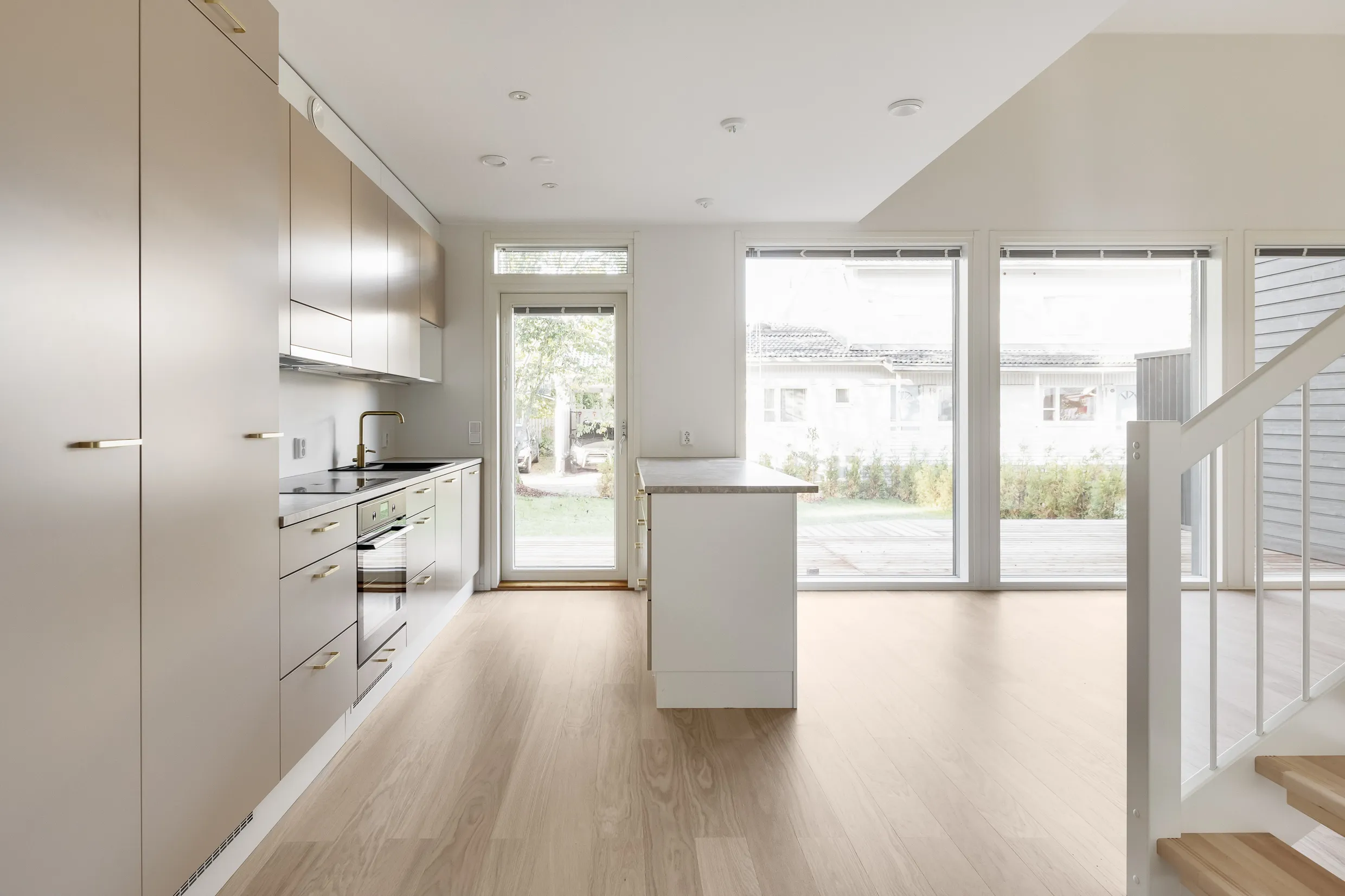 Vaaleassa huoneessa on keittiö, saareke, suuret ikkunat ja portaat.