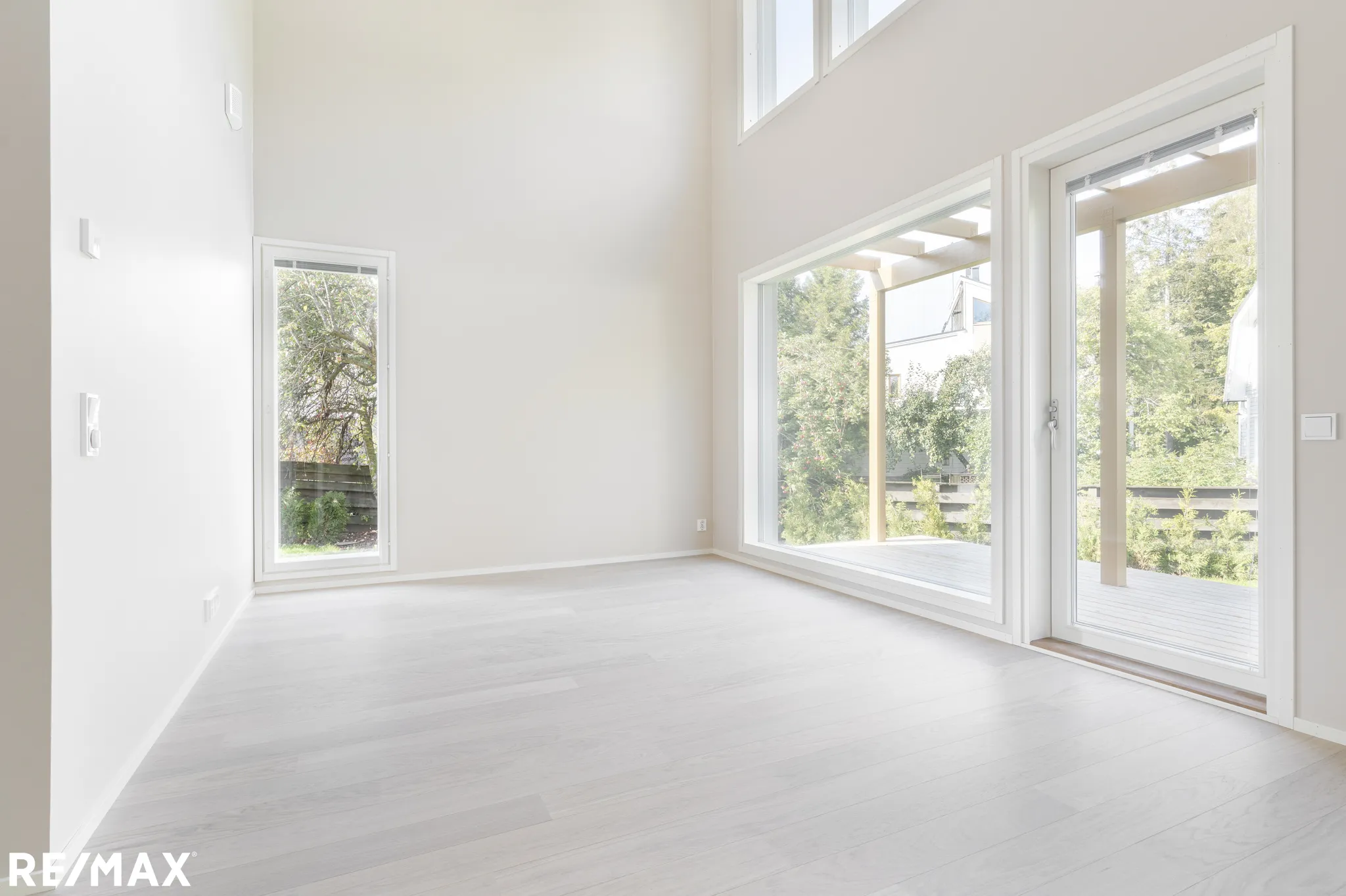 Vaalea, tyhjä huone, jossa on suuret ikkunat ja valkoiset seinät sekä vaalea puulattia.